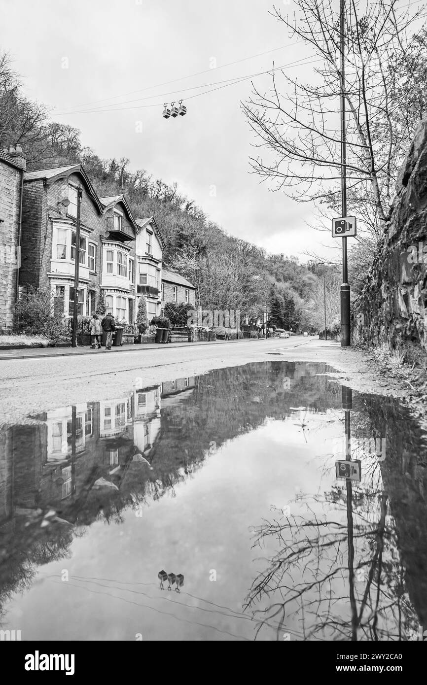 Drei der Seilbahnkabinen der Heights of Abraham spiegeln sich in einer Pfütze zwischen der Straße und dem Fluss Derwent in Matlock Bath, Derbyshire, am 20. April Stockfoto