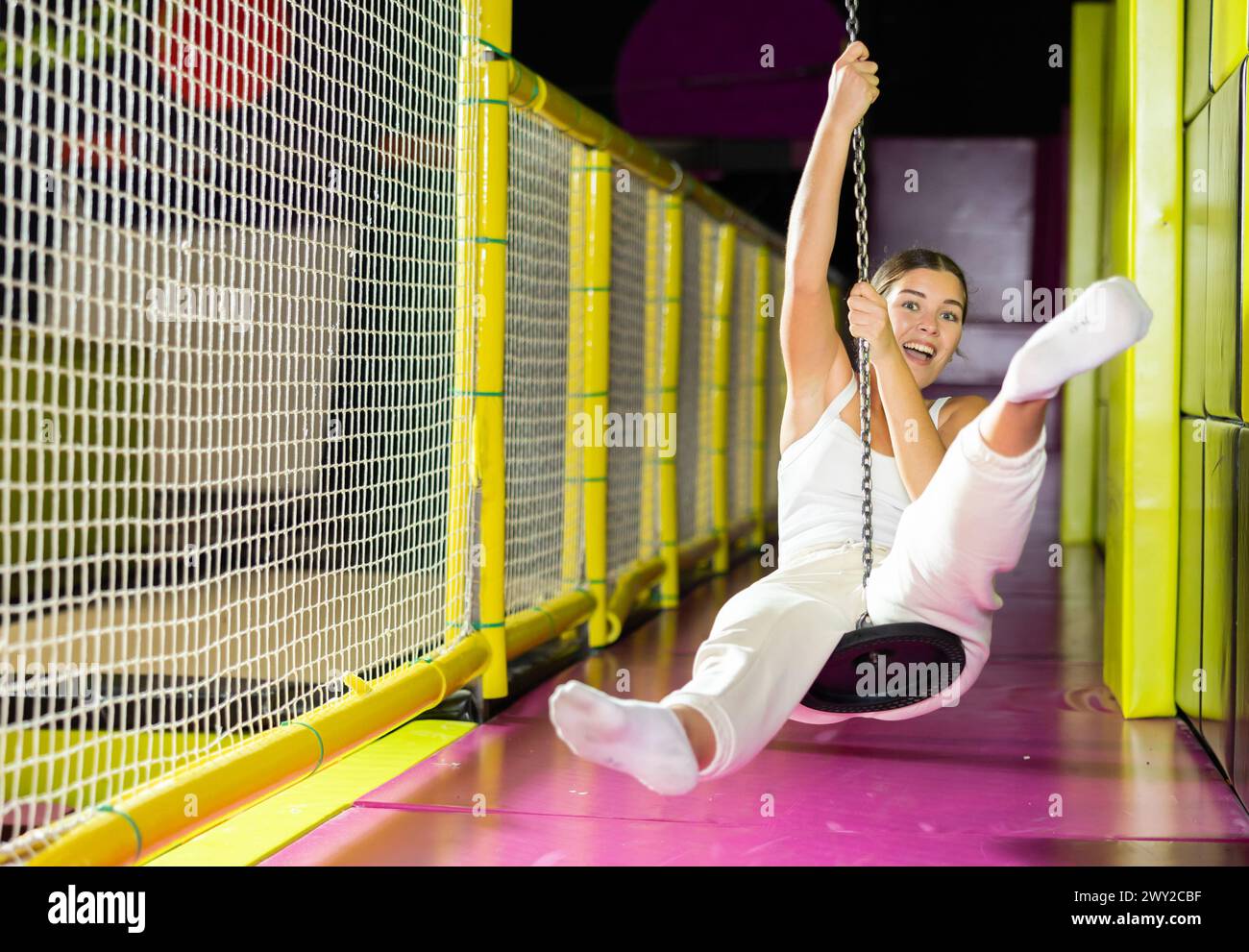 Fröhliches Mädchen, das auf der Seilrutsche im Spielcenter schwingt Stockfoto