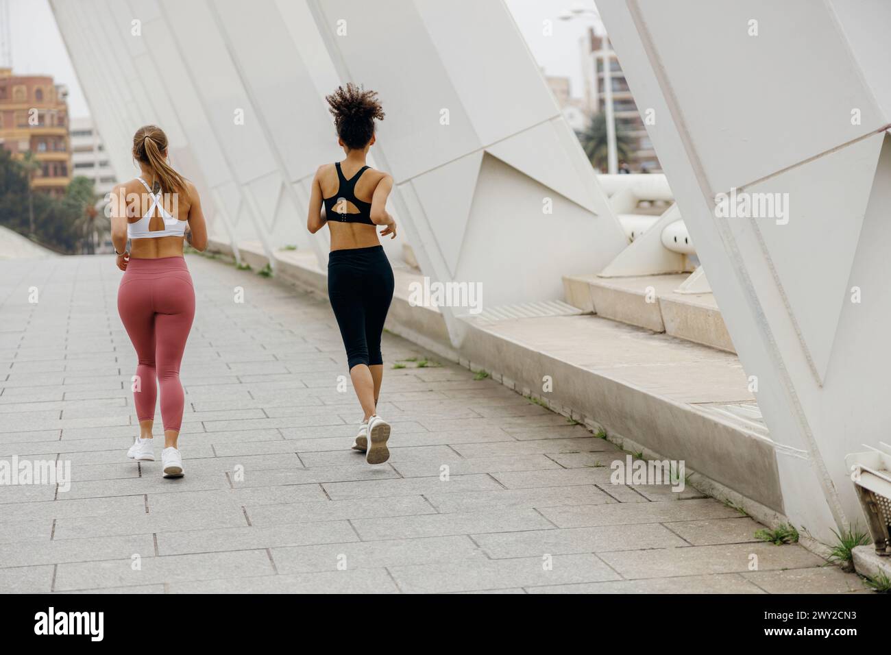 Rückansicht von Frauen, die Seite an Seite auf einer Outdoor-Strecke auf dem Hintergrund von Gebäuden laufen Stockfoto