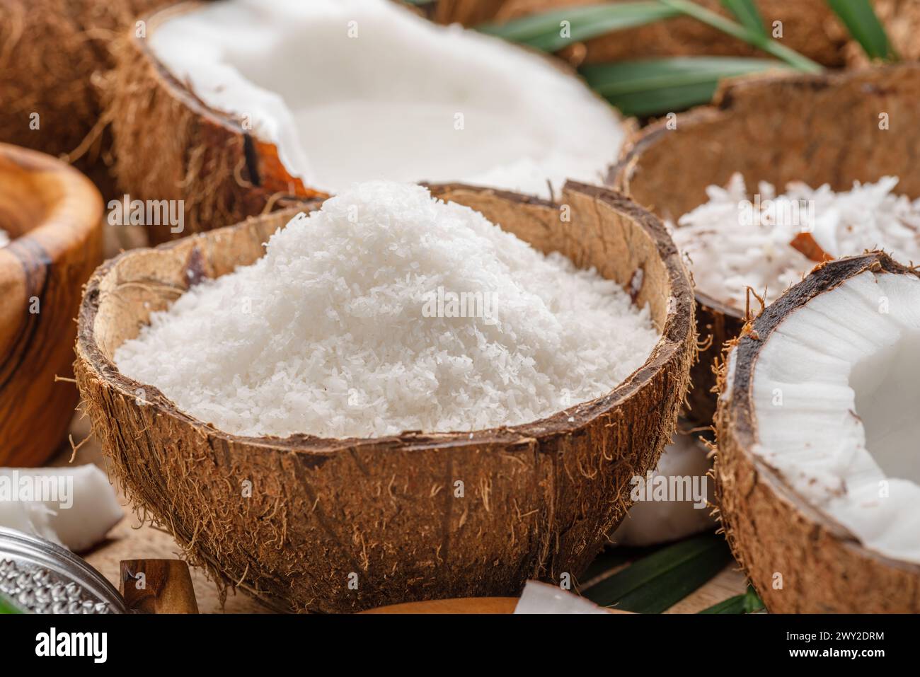 Frisch geöffnete Kokosnüsse zusammen mit Kokosscheiben, Flocken und Kokosblättern auf einem Holztisch. Schöner Hintergrund für Ihre Projekte. Stockfoto