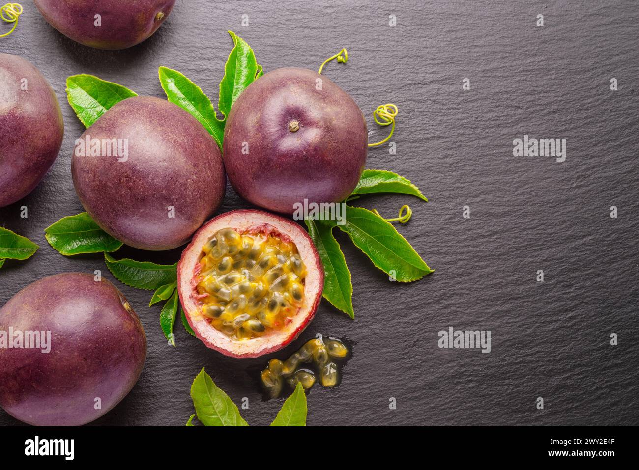 Dunkelviolette Passionsfrüchte und die Hälfte der Maracuya-Frucht isoliert auf Schiefergraphit-grauem Hintergrund. Stockfoto