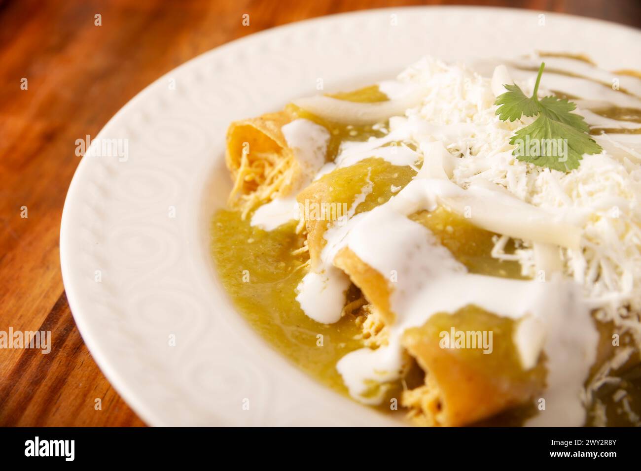 Grüne Enchiladas. Typisches mexikanisches Gericht mit einer gefalteten oder gerollten Maistortilla, gefüllt mit gehacktem Huhn und bedeckt mit würziger grüner Sauce, cre Stockfoto