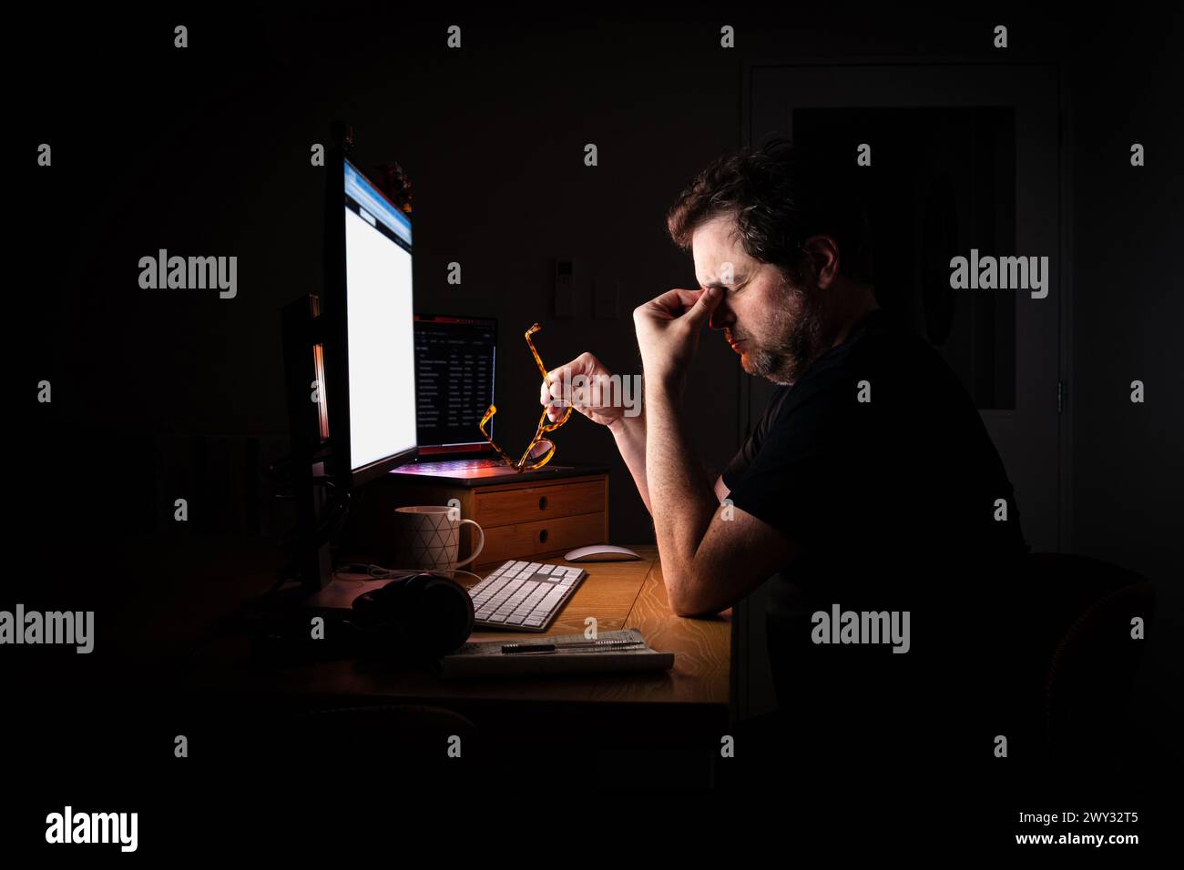 Müde und gestresste Büroangestellte, die nachts in einem dunklen Raum durch das Leuchten ihres Computerbildschirms beleuchtet werden, während sie bis spät arbeiten. Burn Out. Stockfoto