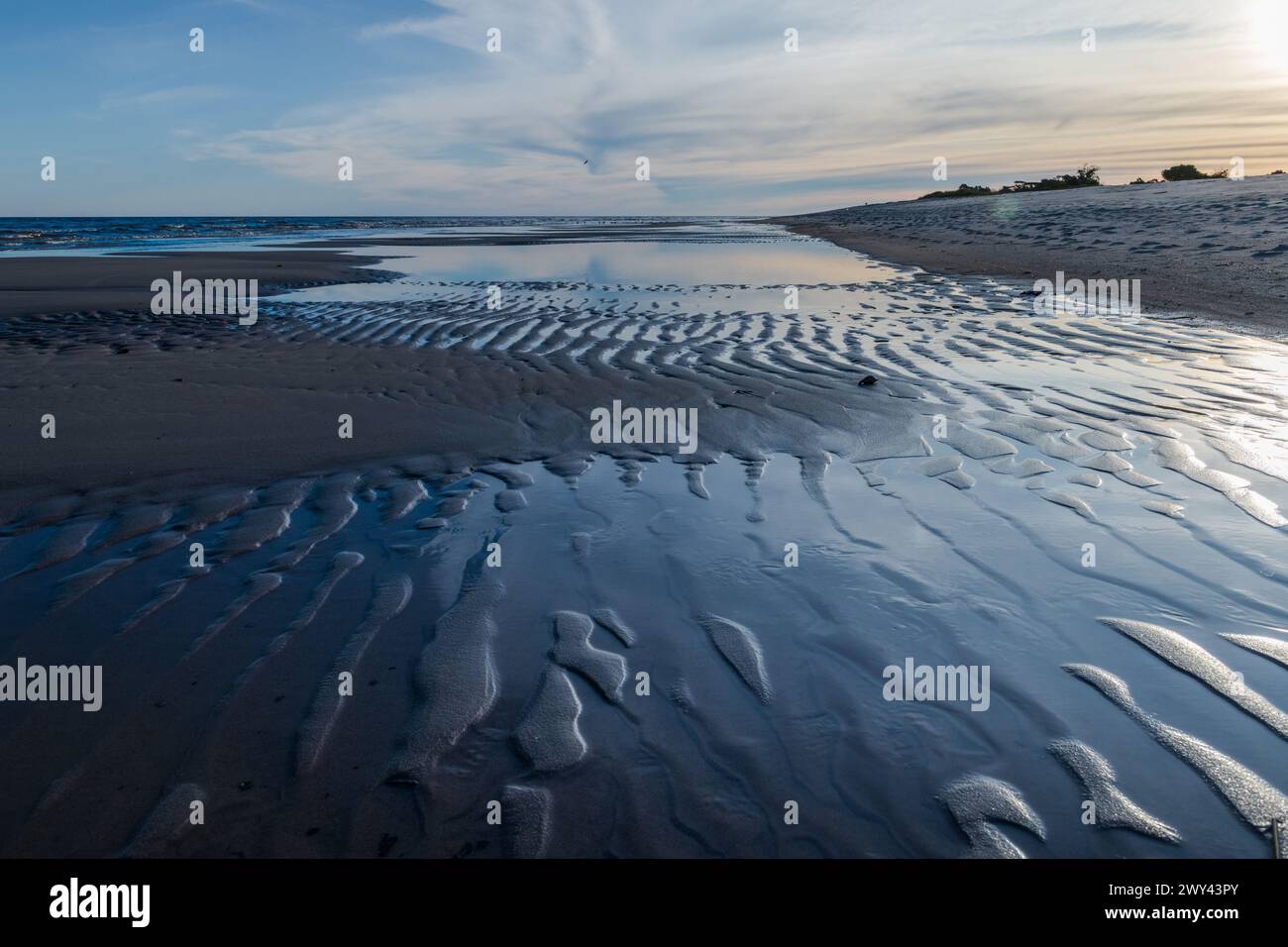 Das Bild ist von einem Strand mit einer Sandküste. Der Sand ist von kleinen Wellen bedeckt, die den Eindruck eines sanften, ruhigen Ozeans erwecken Stockfoto