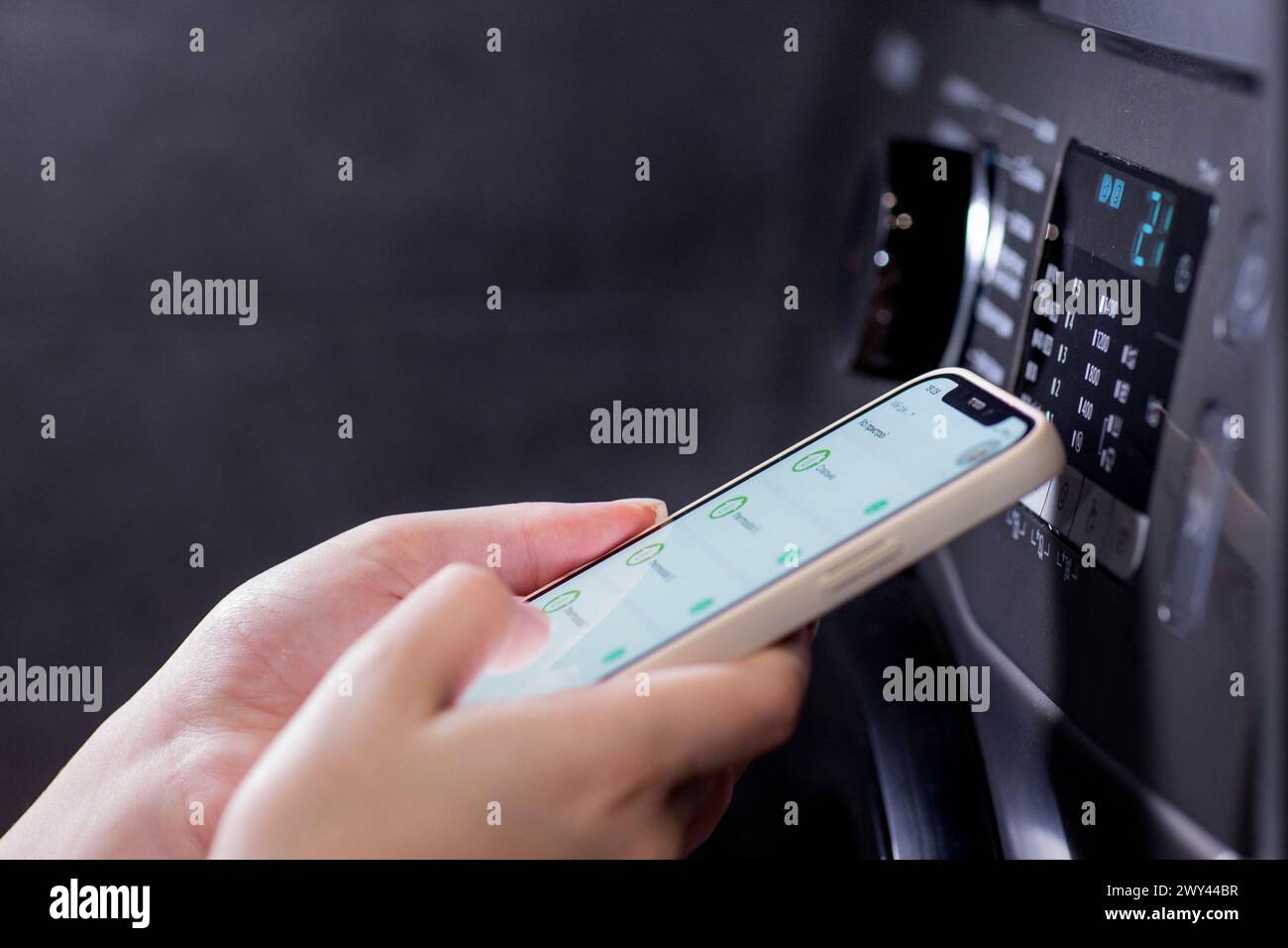 Die Frau steuert die Waschmaschine mit einem Telefon Stockfoto