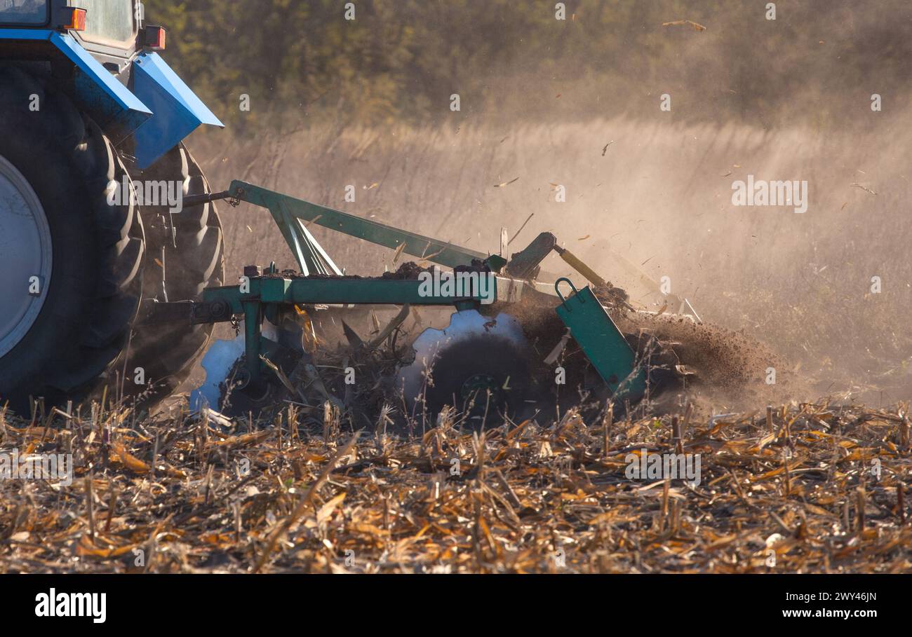 Blauer Traktor pflügt das Feld und entfernt die Reste von zuvor gemähtem Mais. Teil des Grubber, Stahl, runde Scheiben in einer Reihe Nahaufnahme. Arbeiten Sie agrisch Stockfoto