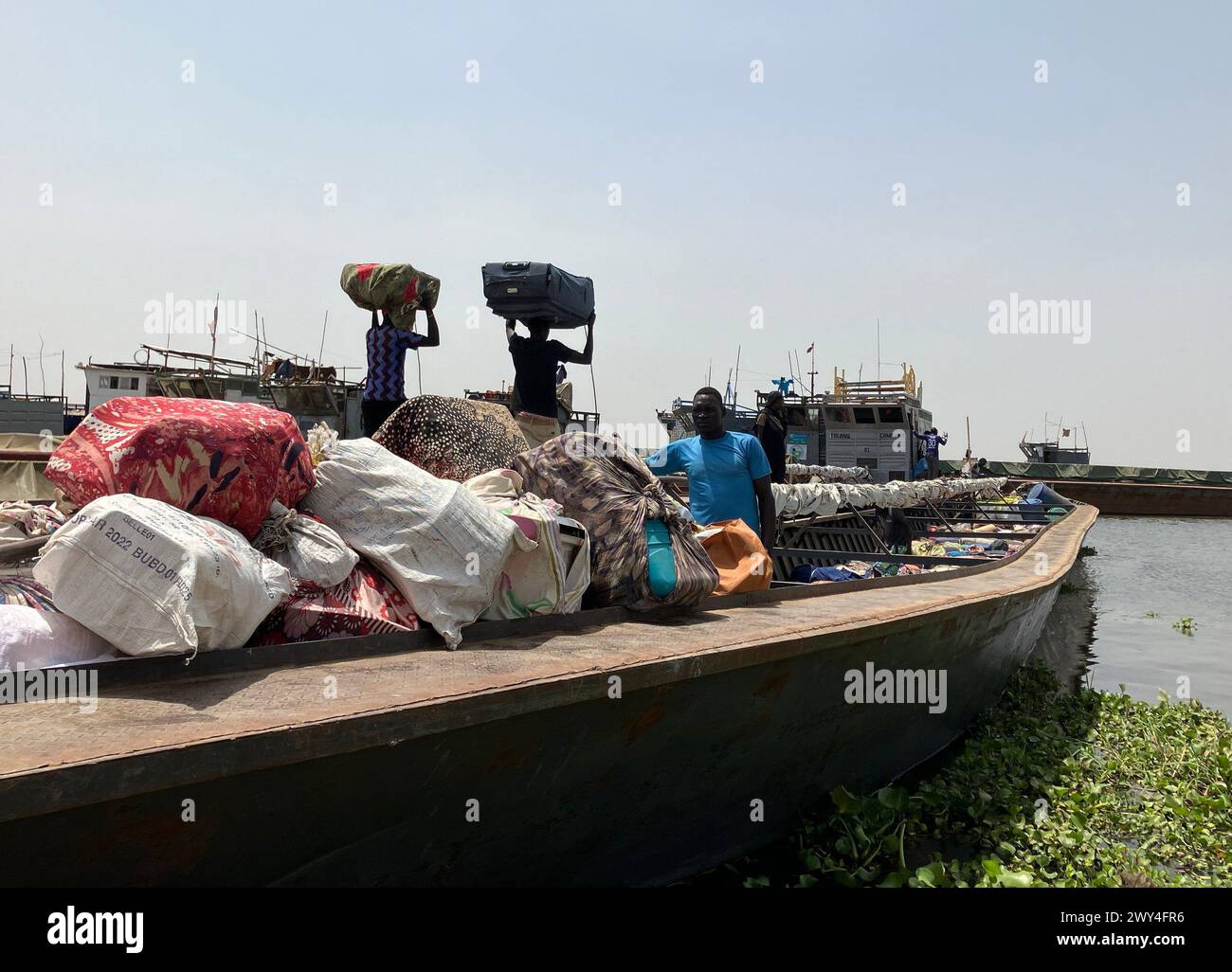 Renk, Südsudan. März 2024. Männer beladen Boote auf dem Weißen Nil, um Flüchtlinge aus dem Sudan aus der Grenzstadt Renk im Südsudan nach Malakal zu bringen. Der blutige Machtkampf im Sudan, der vor einem Jahr begann, hat jetzt die größte Flüchtlingsbewegung der Welt ausgelöst. Mehr als neun Millionen Menschen fliehen vor den Kämpfen im Sudan und in den Nachbarländern. Eva-Maria Krafczyk/dpa/Alamy Live News Stockfoto