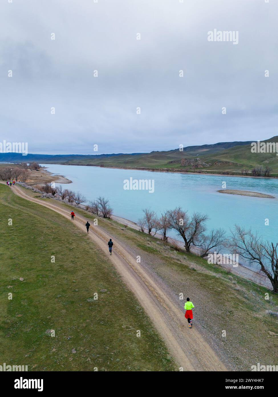 Eine Gruppe von Athleten, die auf einem Pfad entlang eines Gebirgsflusses laufen. Frühe Frühlingszeit, bewölktes Wetter, malerische umliegende Landschaft. Outdoor-Sport Stockfoto
