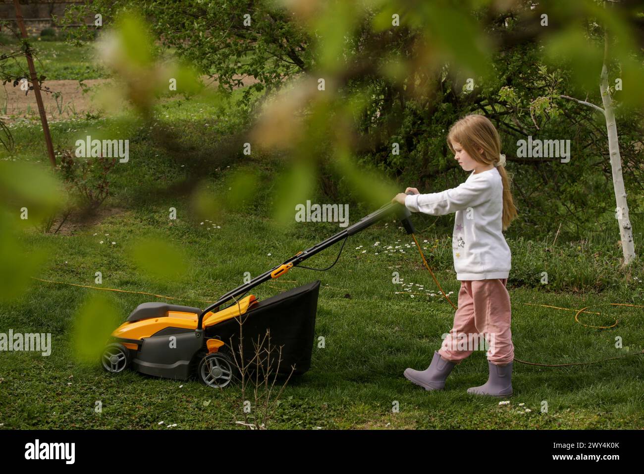 Das kleine Mädchen schneidet Rasen mit dem Mäher und hilft bei Hausarbeiten Stockfoto