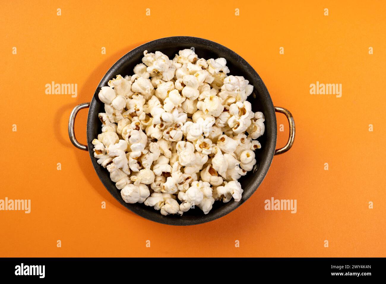 Ein orangefarbener Hintergrund mit einer schwarzen Schale Popcorn. Stockfoto