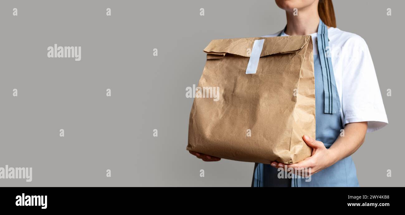 Die Kellnerin hält eine braune Packtasche zum Mitnehmen in ihren Händen. Online-Bestellung für Lebensmittel zum Mitnehmen. Stockfoto
