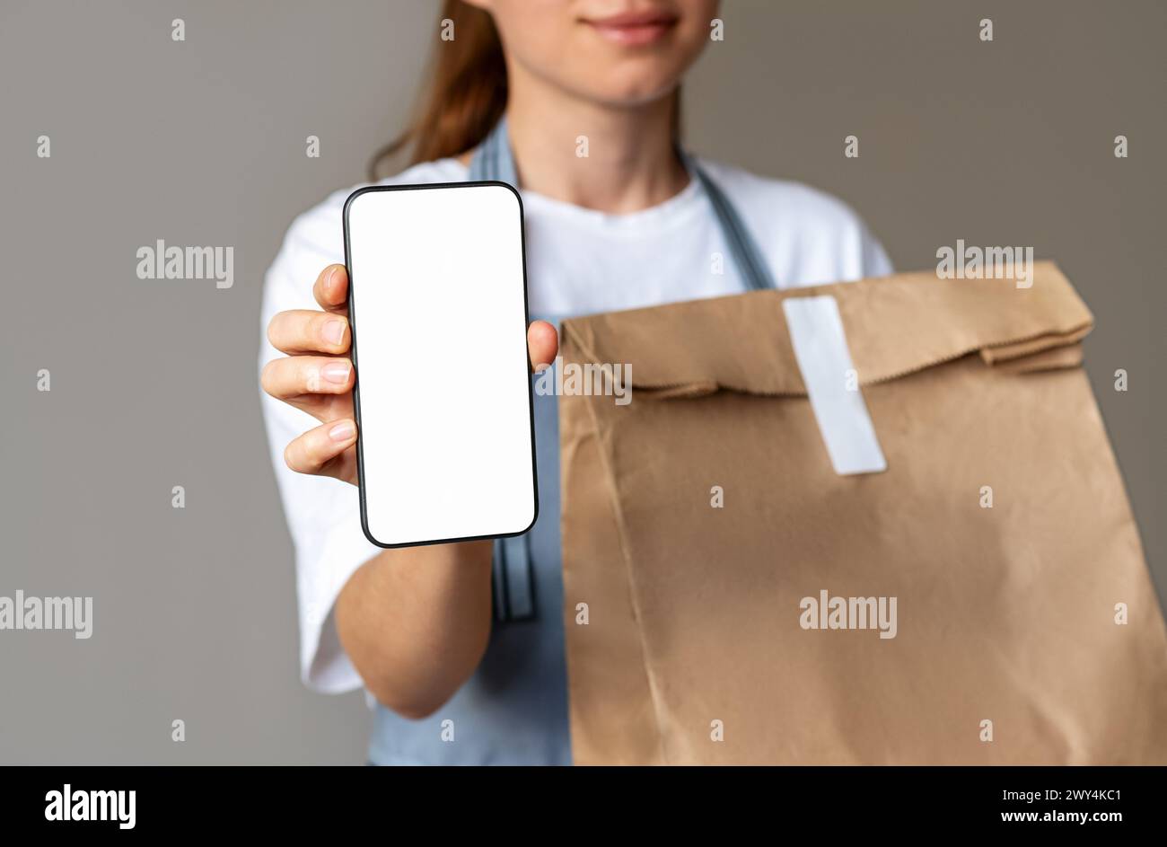 Mockup Mobile App für die Lieferung von Lebensmitteln. Online-Bestellung zum Mitnehmen. Handys- und Papiertüte mit Essen zum Mitnehmen in den Händen der Kellnerin. Take-HOM Stockfoto