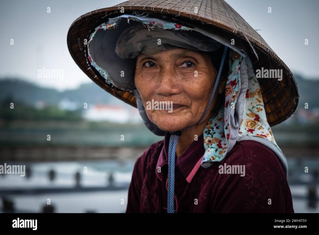 Hart arbeitende vietnamesische ältere Frau in der Salzfarm lächelnd. Porträt lächelnder vietnamesischer Frauen, die einen vietnamesischen Hut tragen. April 1,2024-Nha Stockfoto