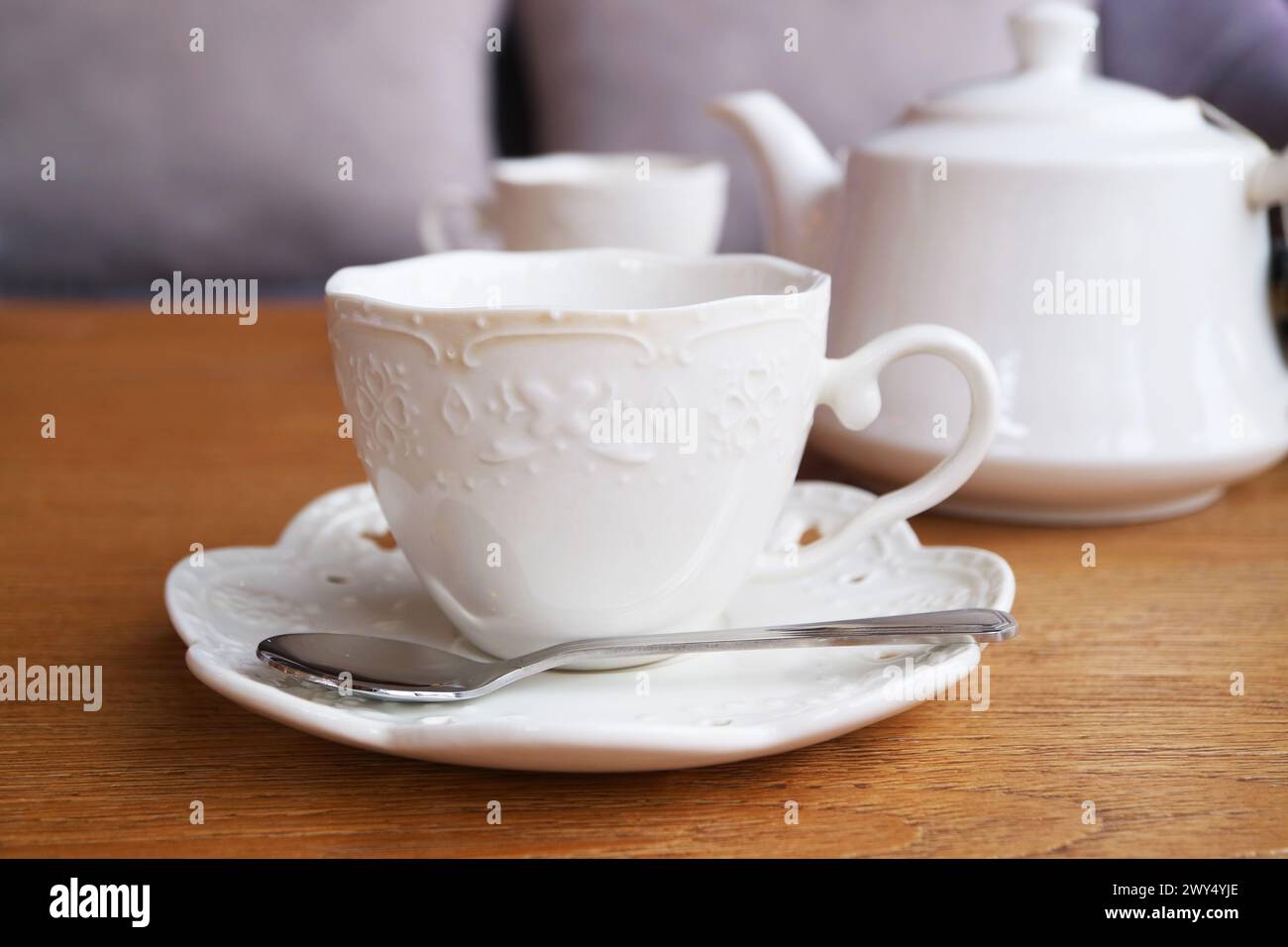 Weiße Tasse mit Tee, die in eine Teekanne im Hintergrund getaucht ist Stockfoto