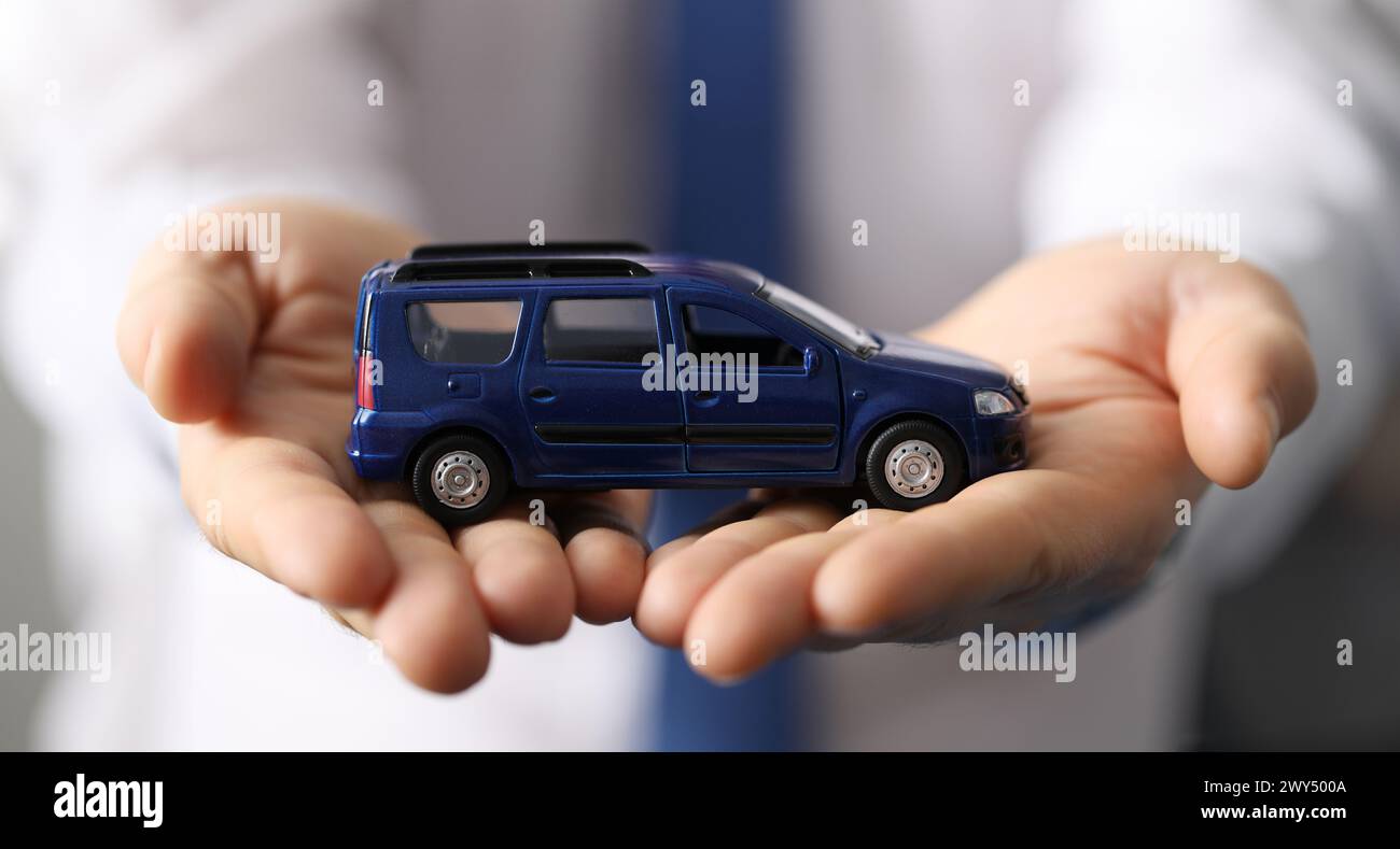In der Nähe hält der Mann im Hemd ein blaues Minivan-Auto für Spielzeug Stockfoto
