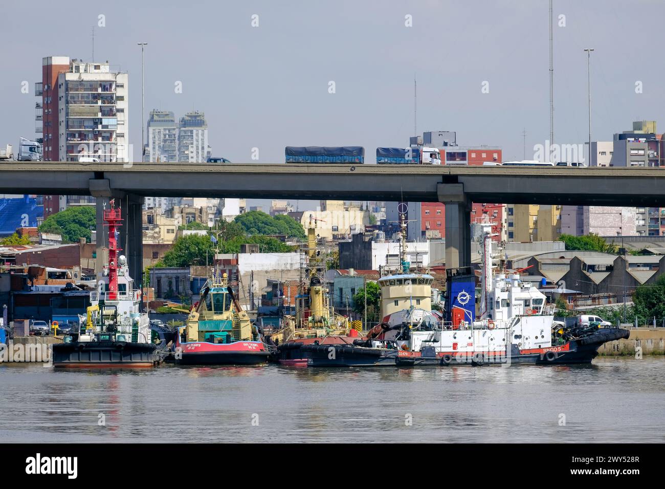 Buenos Aires, Argentinien - Blick auf die Stadt am Hafen mit der Stadtautobahn auf der Puente del Riachuelo, dichten Gebäuden und Motorschlepper davor. Stockfoto