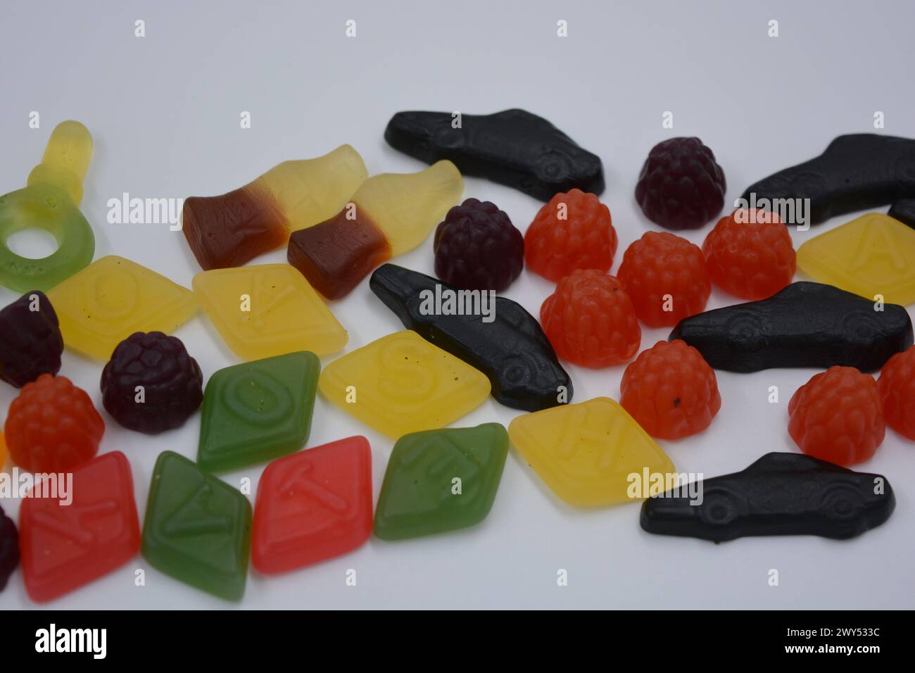 Süßigkeiten in Form eines schwarzen Autos, Himbeeren, Brombeeren, Cola-Flaschen, farbige Schlüssel, Diamanten mit dem Alphabet. Stockfoto