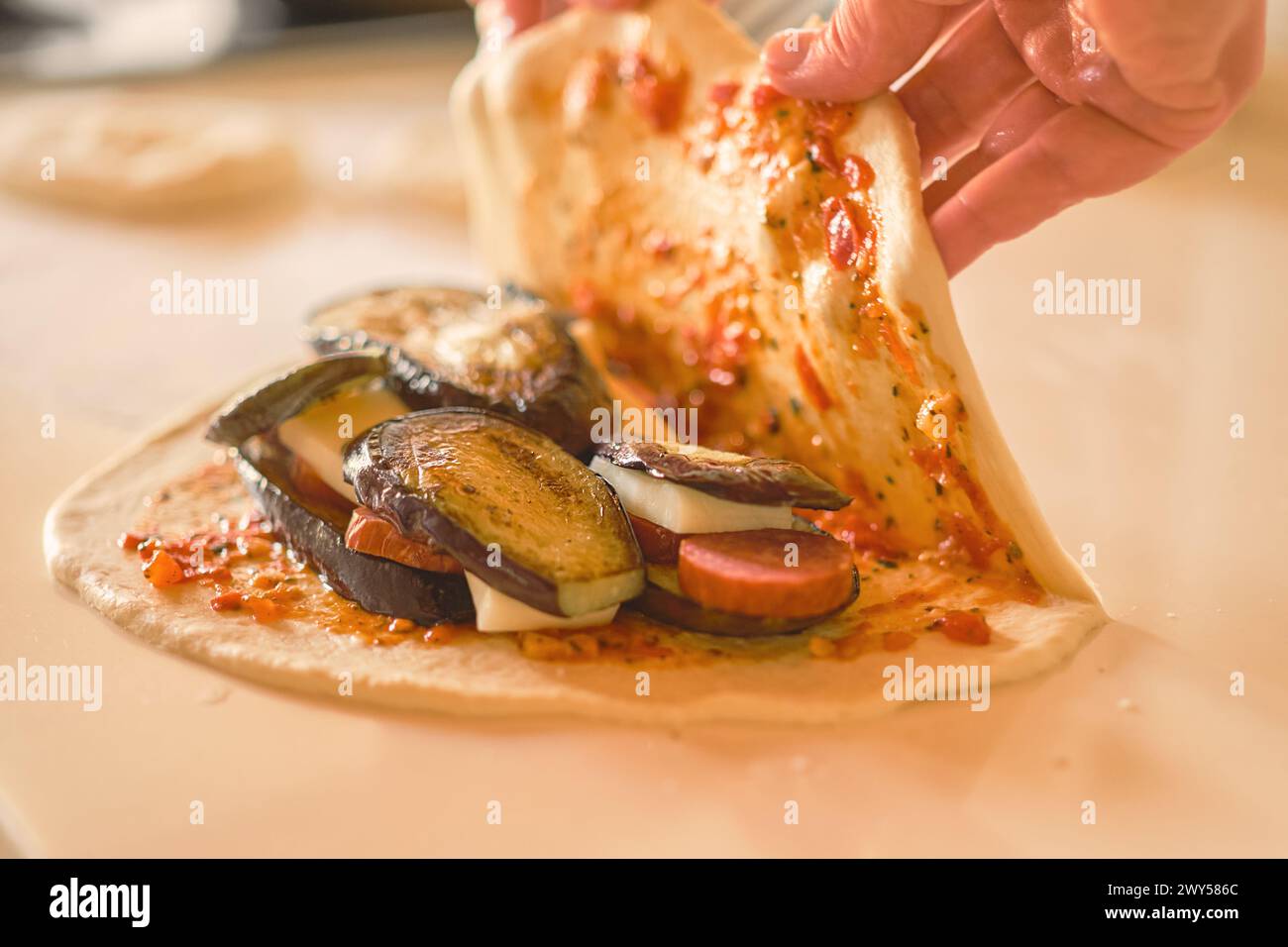 Die Hände des Küchenchefs decken die Zutaten auf dem Teig ab, während Sie traditionelle italienische Gerichte Calzone, selektive Fokussierung und verschwommener Hintergrund zubereiten Stockfoto