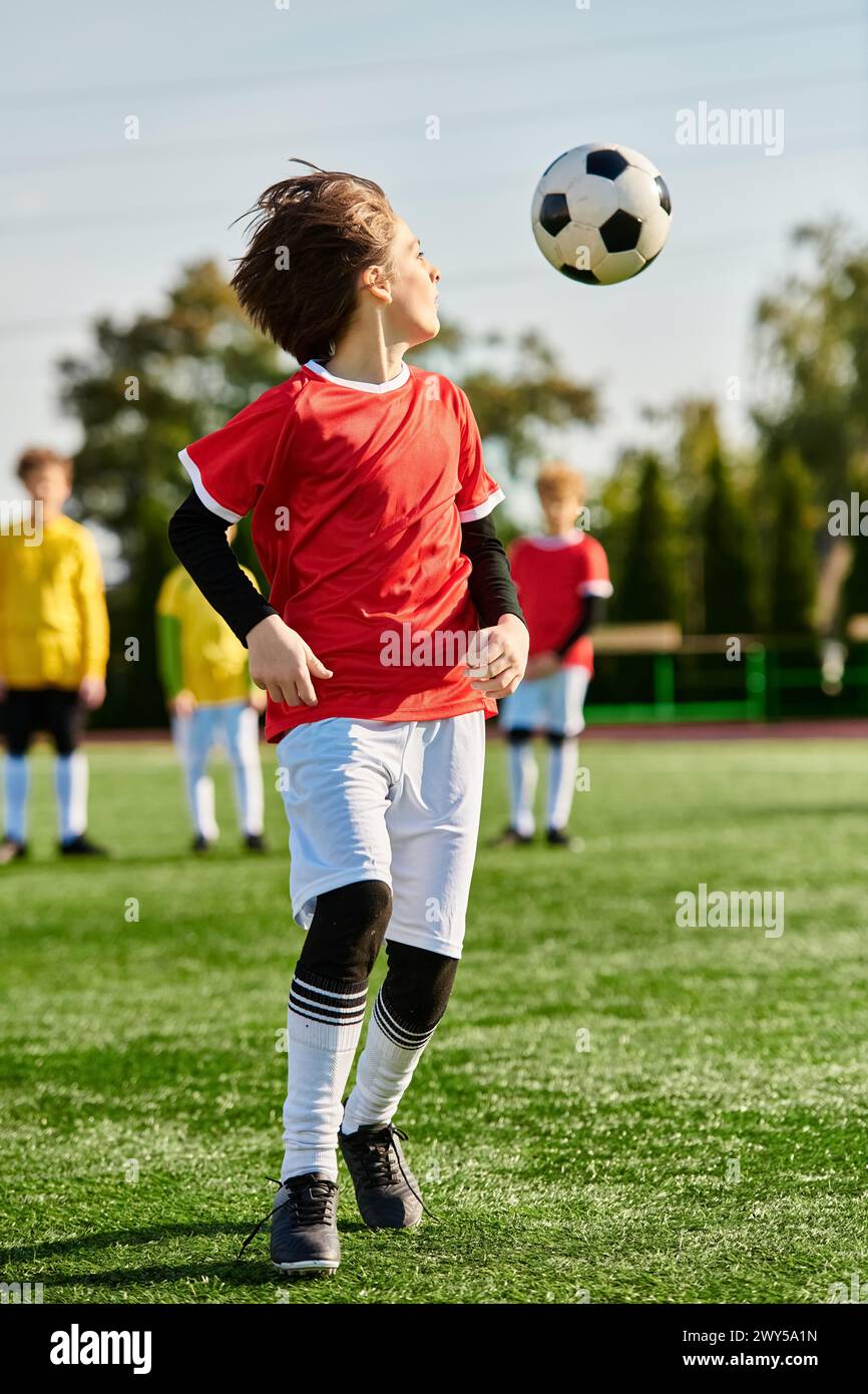 Ein temperamentvoller kleiner Junge spielt energisch auf einem grasbewachsenen Feld Fußball und dribbelt den Ball geschickt mit zielgerichteter Entschlossenheit an imaginären Gegnern vorbei. Stockfoto