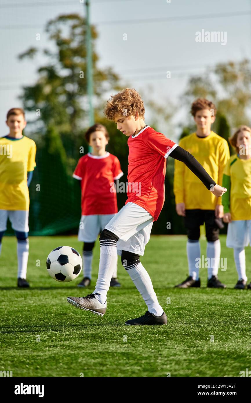 Ein kleiner Junge tritt energisch einen Fußball über ein weitläufiges grünes Feld. Die helle Sonne wirft lange Schatten, während er den Ball geschickt manövriert Stockfoto