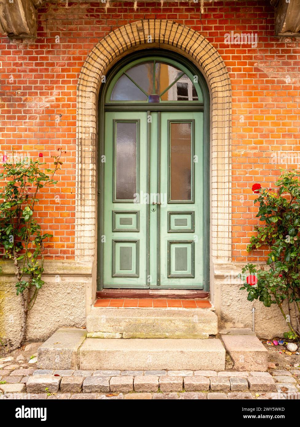 Vorderansicht der bezaubernden grünen Tür mit Bogen und Rosen in der Altstadt von Mariager, Nordjylland, Dänemark Stockfoto
