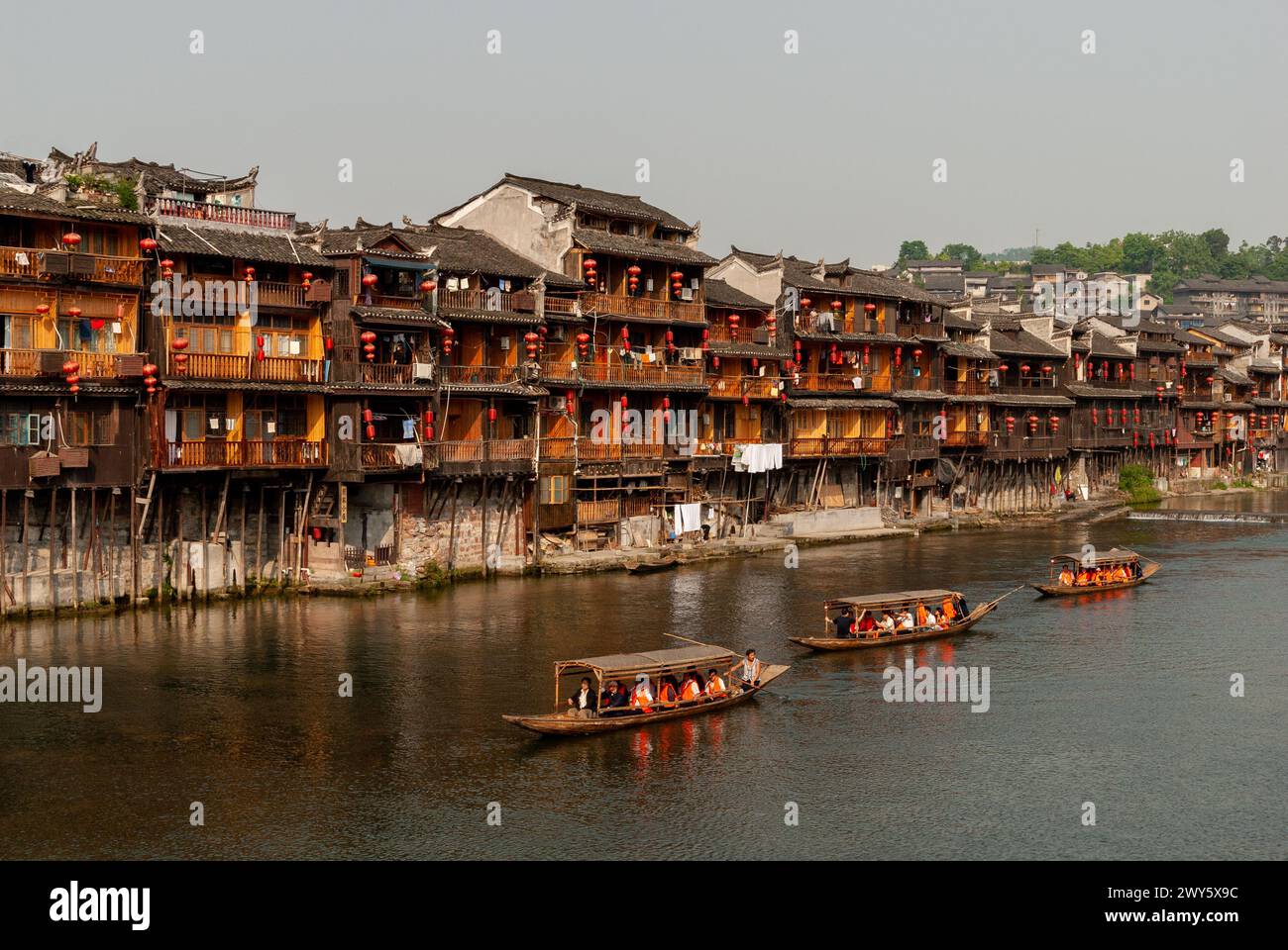 Touristenboote passieren die alten Holzgebäude am Ufer des Flusses in Fenghuang, einer antiken Stadt in Hunan, China. Mai 2008. Stockfoto