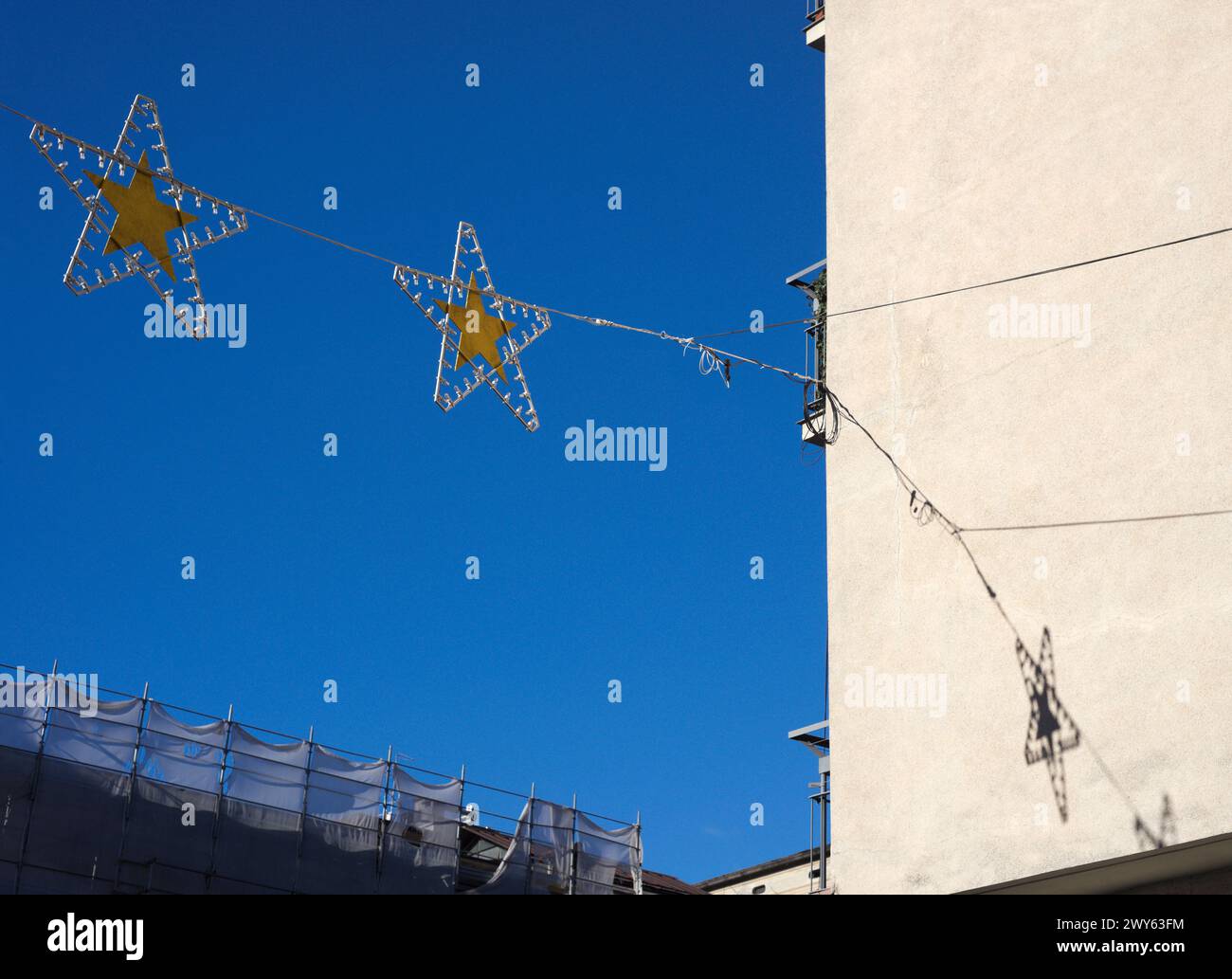 weihnachtssterndekorationen hängen vor einer Gebäudewand über der Straße Stockfoto