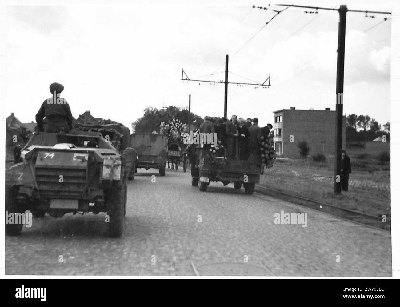Während des Vormarsches der Infanterie-Brigaden passiert ein Konvoi der britischen Armee eine Beerdigung in Antwerpen, die die Truppenbewegungen und die militärische Präsenz der 21. Armeegruppe in Belgien veranschaulicht. Stockfoto