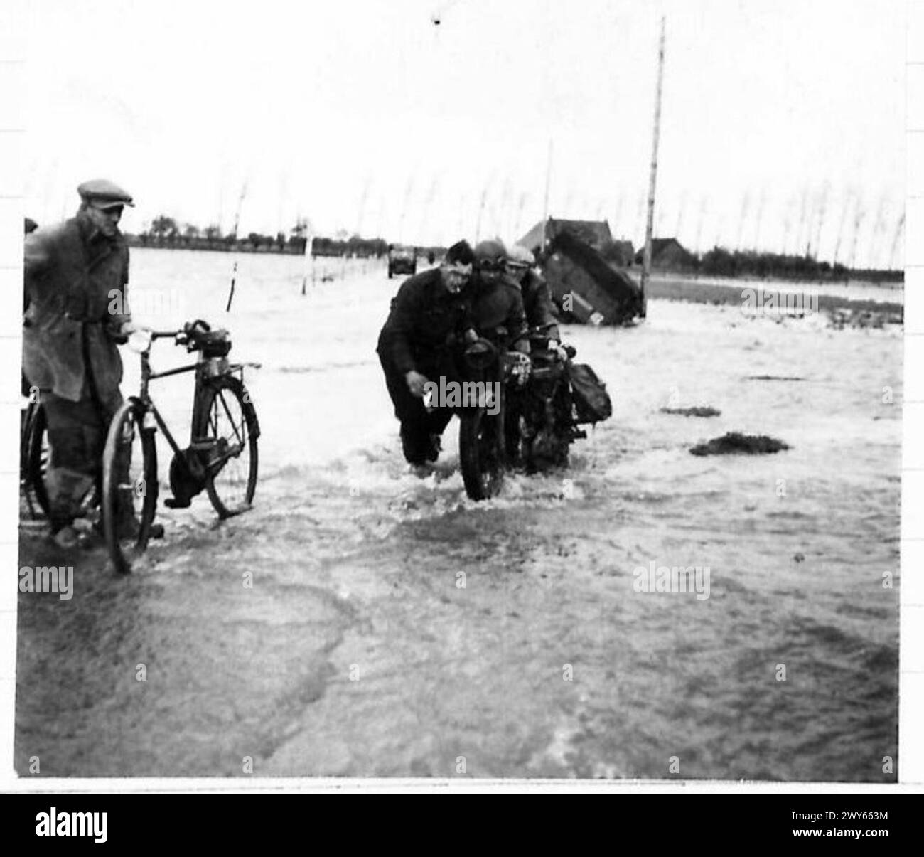 Ein Entsendefahrer wird von Truppen der britischen Armee und Zivilisten unterstützt, um sein Motorrad während der Operationen der 21. Armeegruppe aus den Überschwemmungen in Holland zu bergen. Stockfoto