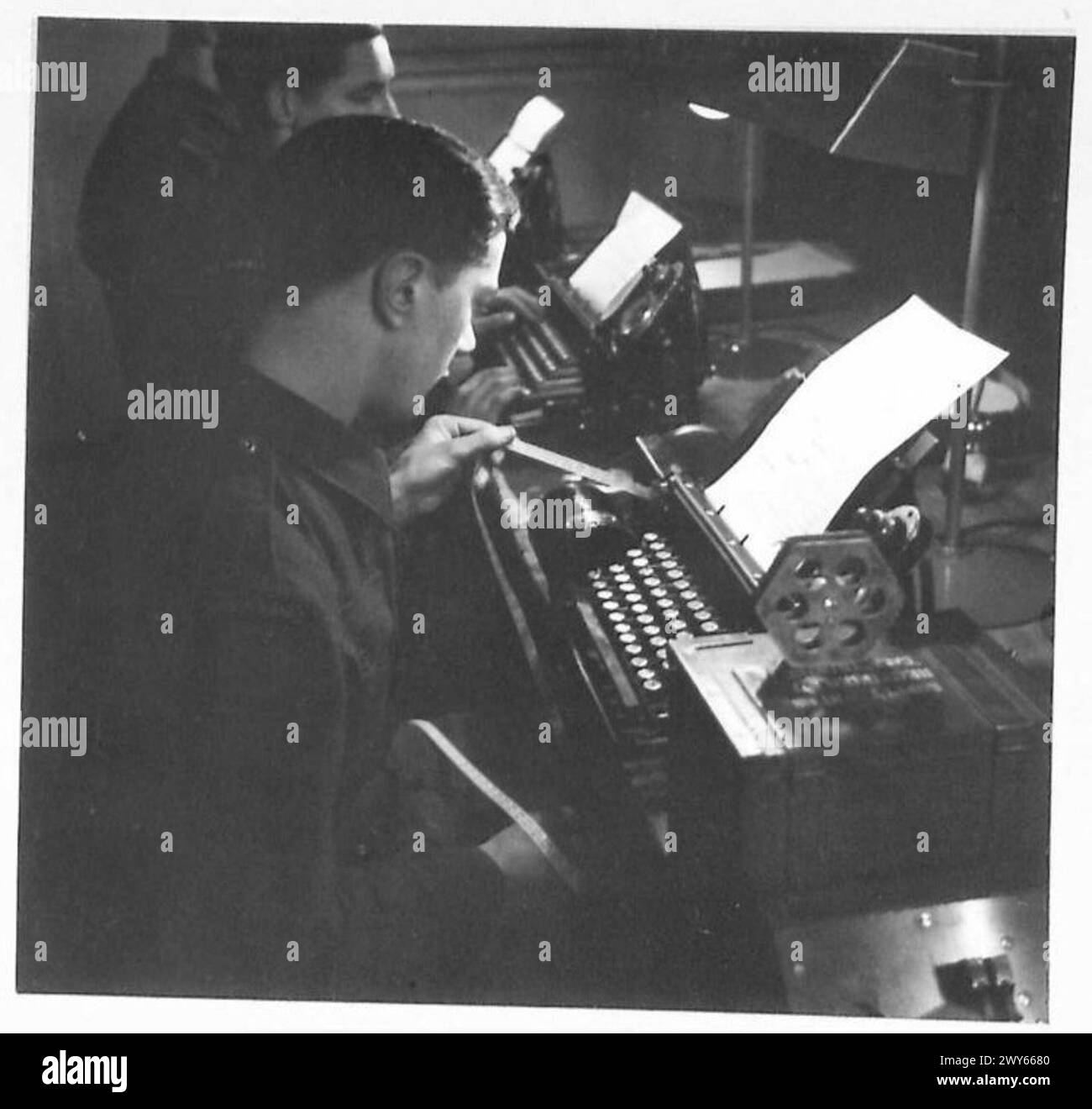 Signalmann Holbrook untersucht perforierte Klebebänder, die in Telekommunikations- oder Datenaufzeichnungsvorgängen verwendet werden. Britische Armee, 21. Armeegruppe. Stockfoto