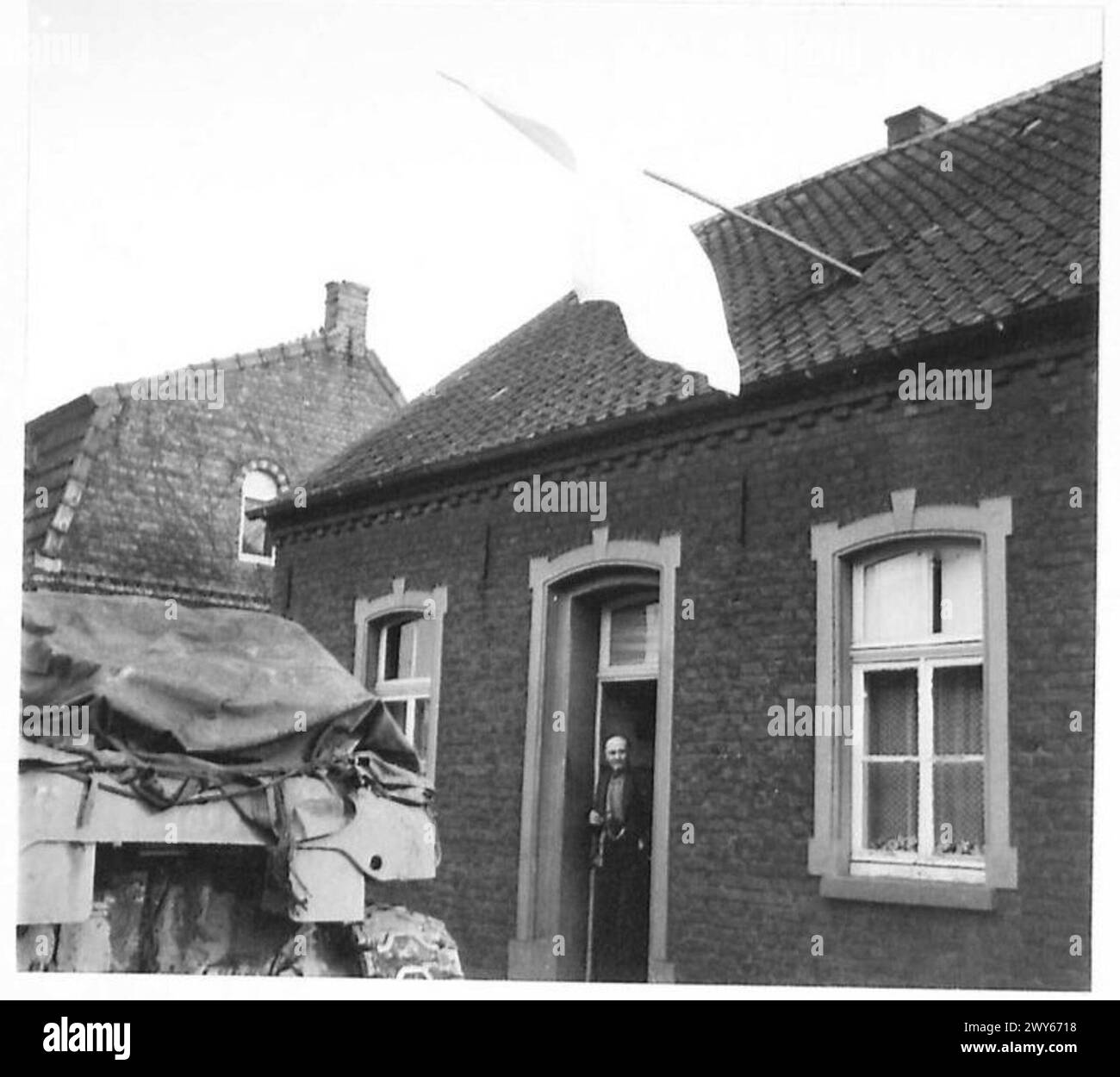 Ein Zivilist stand vor seiner Tür mit einer weißen Flagge, die auf die Kapitulation oder den Status eines Nichtkämpfers hinwies, während Operationen mit der britischen Armee, der 21. Armeegruppe, durchgeführt wurden. Stockfoto