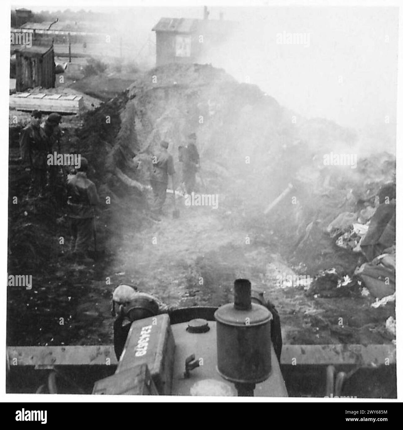 KZ BELSEN - die alten befallenen Lappen werden verbrannt und dann mit Hilfe eines Bulldozers begraben. Britische Armee, 21. Armeegruppe Stockfoto