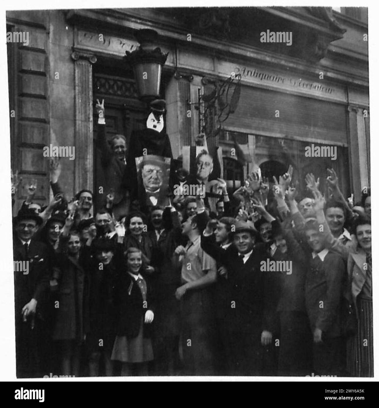 Die Belgier zeigen Siegeszeichen vor einem Quisling-Haus, mit einem Bildnis von Hitler und Frauen, die Porträts von Churchill und Roosevelt während der Operationen der britischen Armee 21st Army Group in Nordwesteuropa halten. Stockfoto