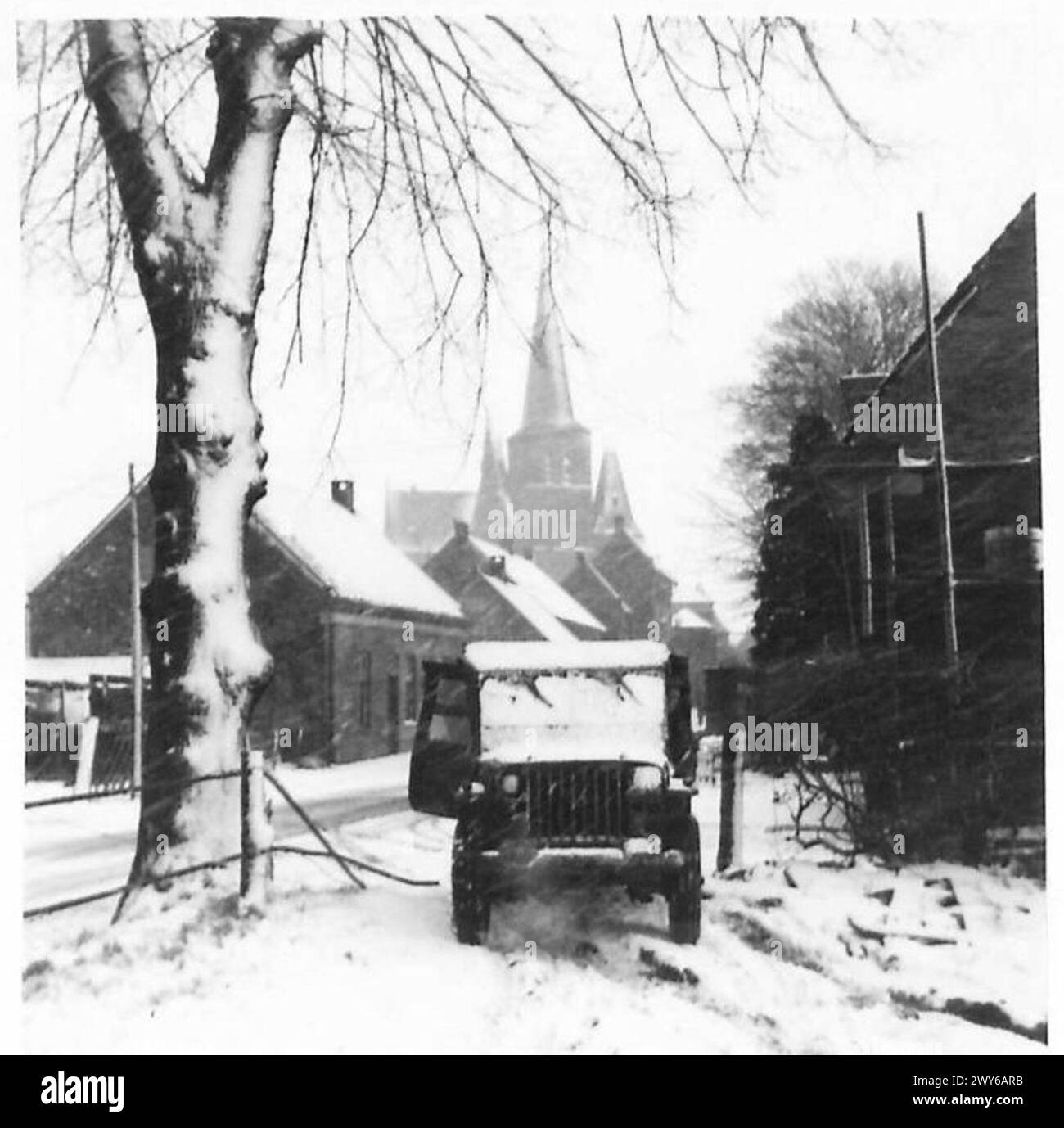 Ein Jeep der britischen Armee bewegt sich während der Wintereinsätze in Holland durch schneebedeckte Straßen in einem niederländischen Dorf, 21. Armeegruppe. Stockfoto