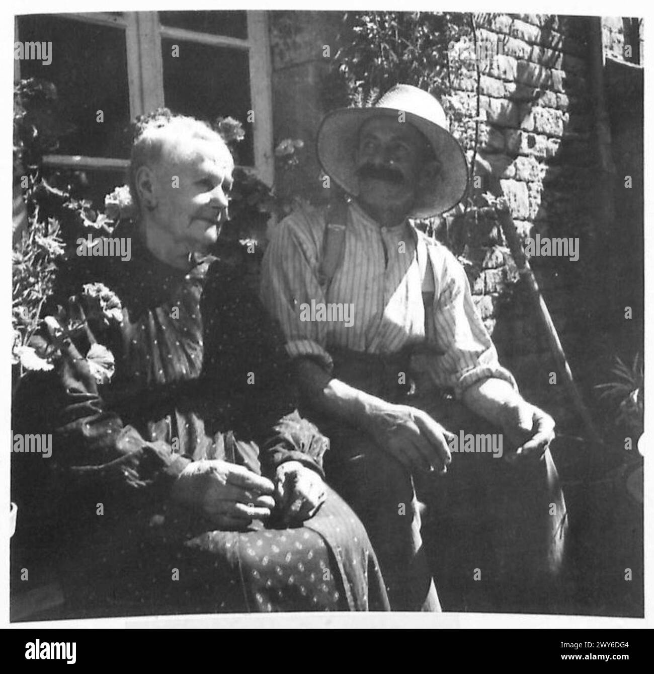 Ein französisches Paar genießt den Sonnenschein vor ihrem Dorfhaus und spiegelt das tägliche Leben in einem französischen Dorf während der Operationen der britischen Armee 21st Army Group wider. Stockfoto