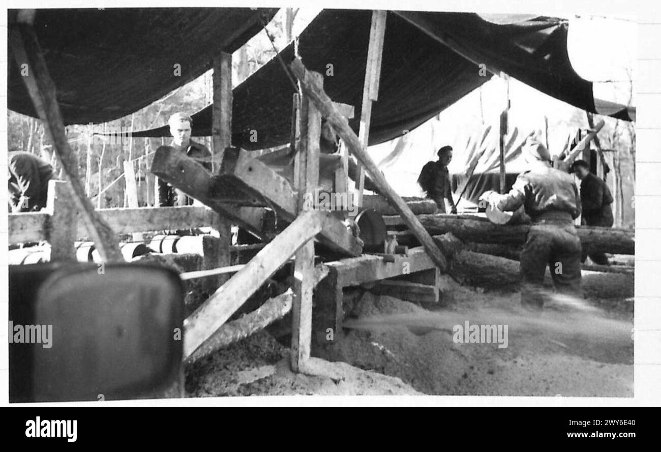 Ein mit abgeschnittenen Stämmen beladener Panzertransporter wird an einer niederländischen Ladebucht durch einen Bulldozer vom Schlamm befreit, was die Logistik der 21. Armee der britischen Armee in Holland nach der Befreiung veranschaulicht. Stockfoto