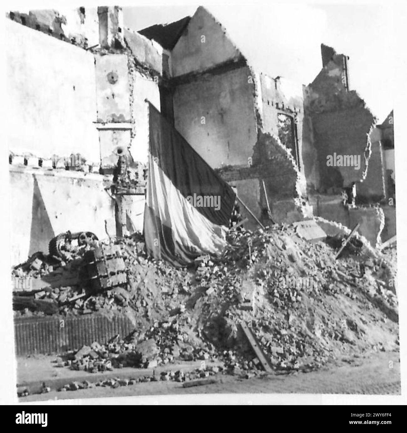 Ein belgischer Hausherr legt eine belgische Flagge auf die Ruinen der Häuser, die in der Schlacht von Gheel zerstört wurden, und symbolisiert den Nationalstolz und die Auswirkungen des Kampfes während der Operationen der britischen Armee, 21. Armeegruppe. Stockfoto