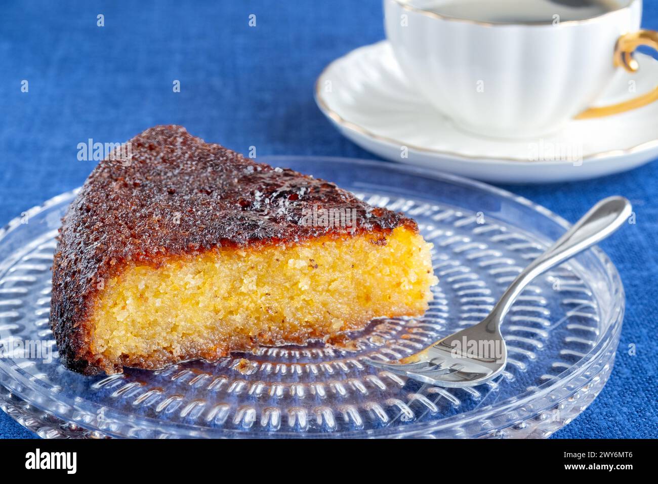 Bristol, Großbritannien. Eine einteilige Portion eines Mandelzitruskuchen, serviert auf einem Teller mit einer heißen Tasse Kaffee auf einem Tisch, der mit einer blauen Tischdecke bedeckt ist Stockfoto