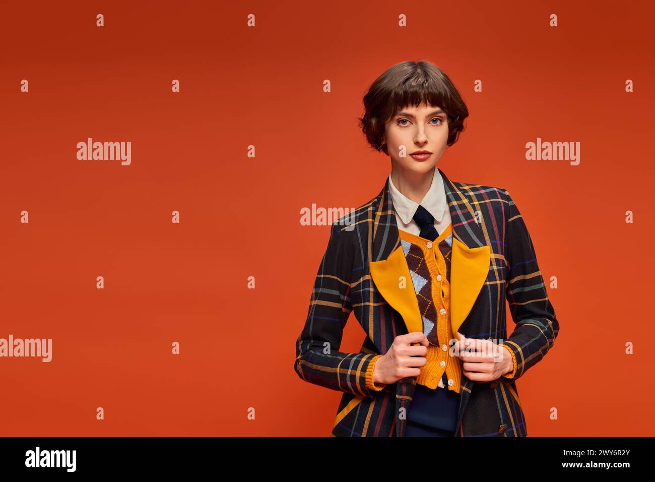 Stylischer Student mit kurzen Haaren in kariertem Blazer auf orangefarbenem Hintergrund, College-Uniform Stockfoto