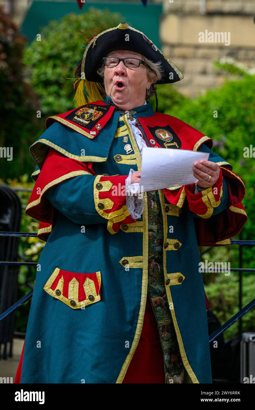 Weibliche Stadtschreierin (bunte geflochtene Schreieruniform) proklamiert, macht laute öffentliche Proklamation und Ankündigung - Ilkley, West Yorkshire England Großbritannien. Stockfoto