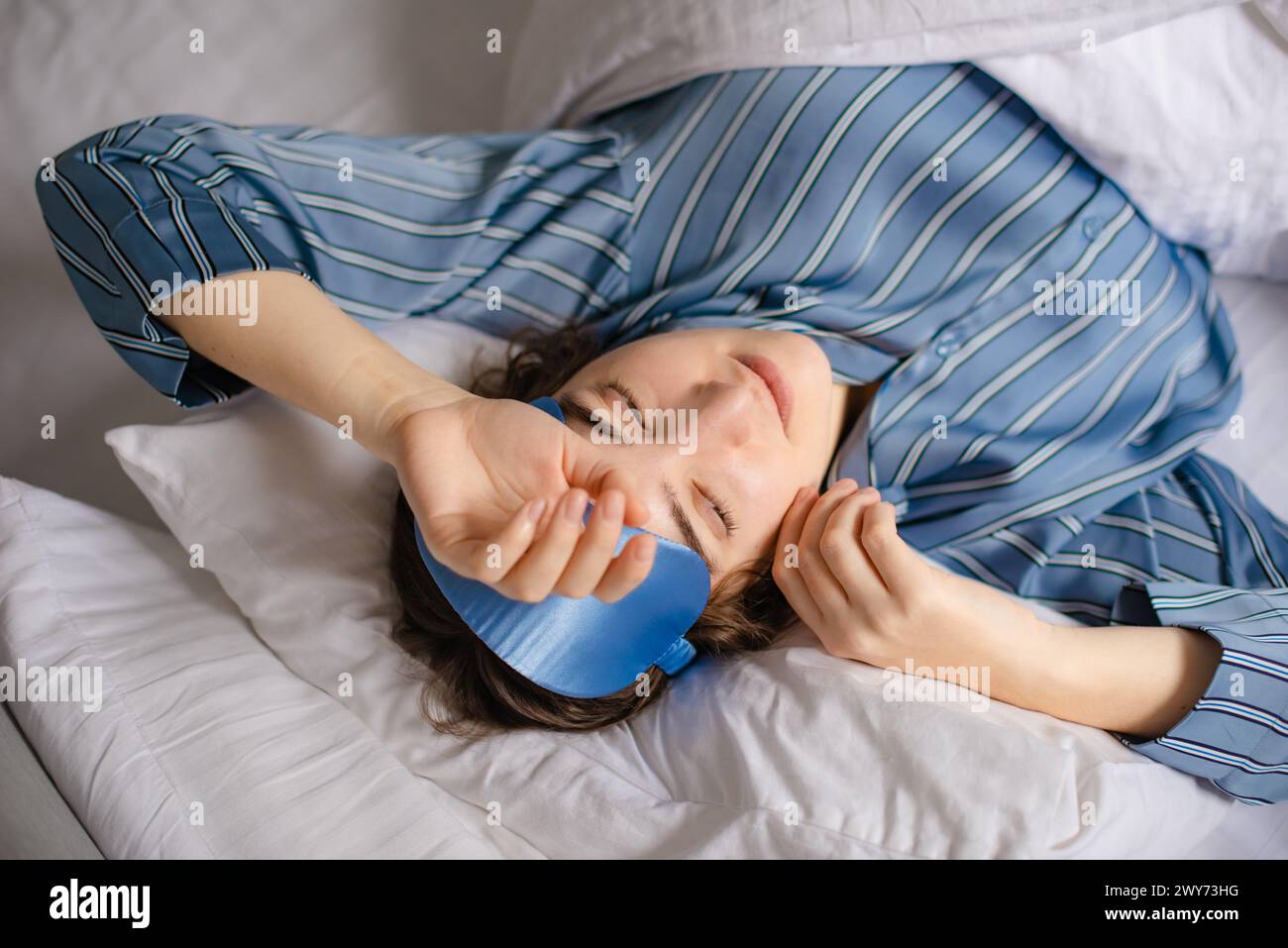 Die Frau entfernt morgens die blaue Seidenschlafmaske von ihren Augen Stockfoto