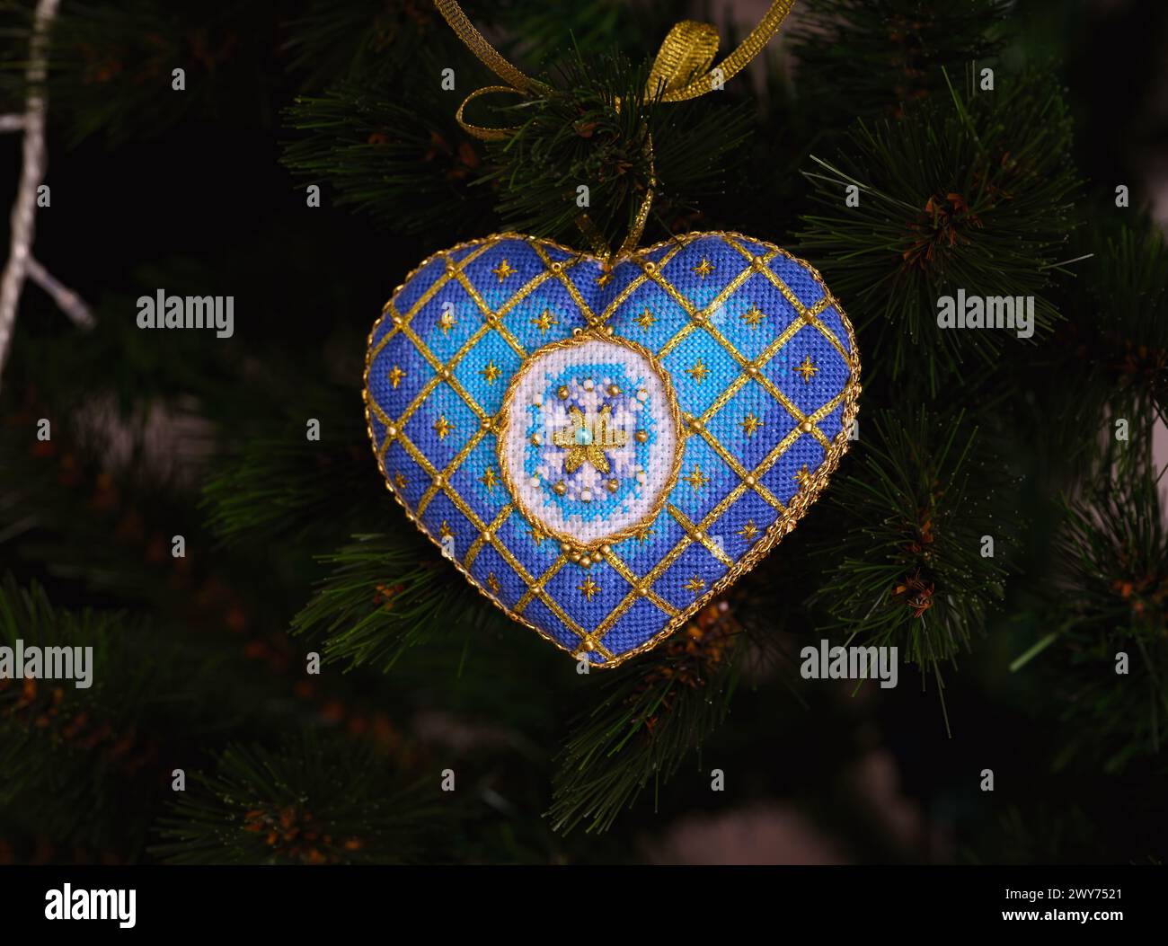 Ein blaues Kreuzstich mit zeitloser Eleganz auf einem Weihnachtsbaum. Dieses blau-goldene Weihnachtsschmuck mit aufgestickter Schneeflocke Stockfoto