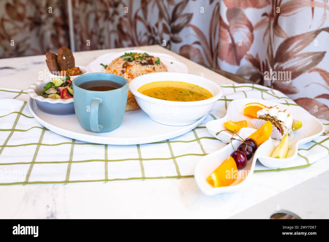Usbekische Nationalgerichte, Plov, Shurpa, Salat und nicht auf einem Tablett mit Tee. Traditionelle usbekische Küche. Hintergrund mit kariertem Tischtuch. Stockfoto