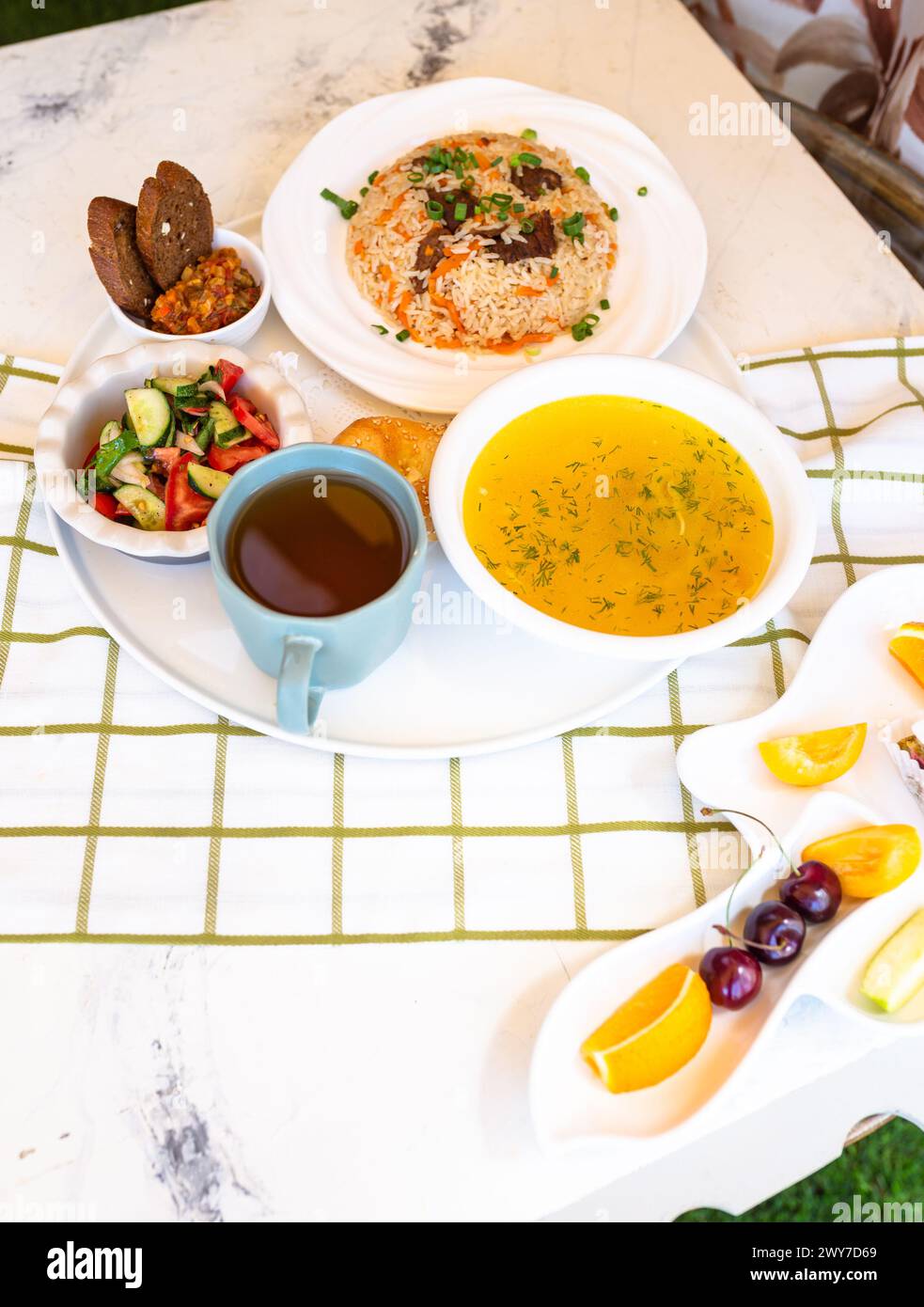 Usbekische Nationalgerichte, Plov, Shurpa, Salat und nicht auf einem Tablett mit Tee. Traditionelle usbekische Küche. Hintergrund mit kariertem Tischtuch. Stockfoto