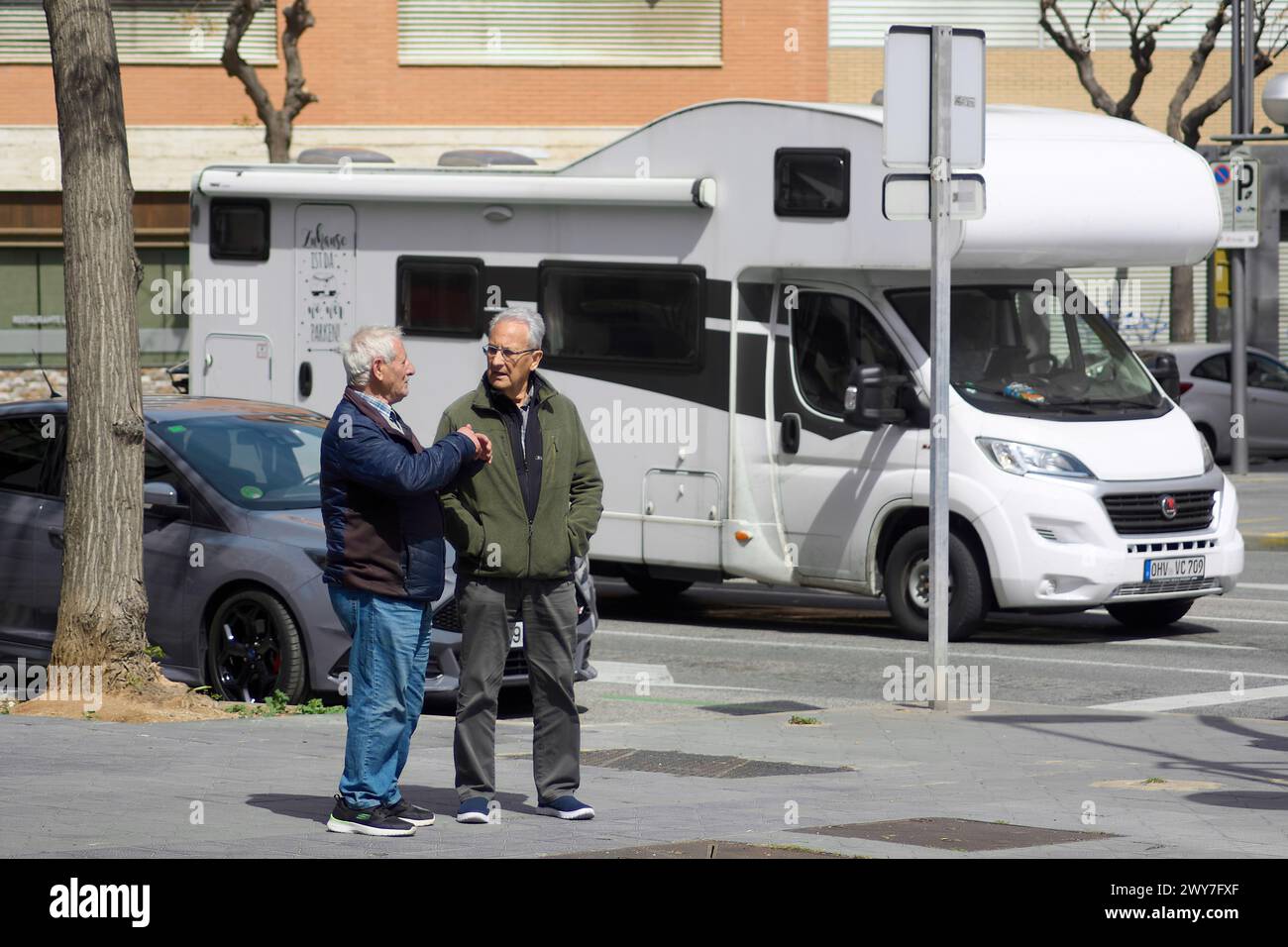 Tarragona, Spanien - 4. April 2024: An einem sonnigen Tag in Tarragona halten zwei Personen an, um sich in der Nähe einer weißen Karawane zu unterhalten und einen Alltagsmoment festzuhalten. Stockfoto