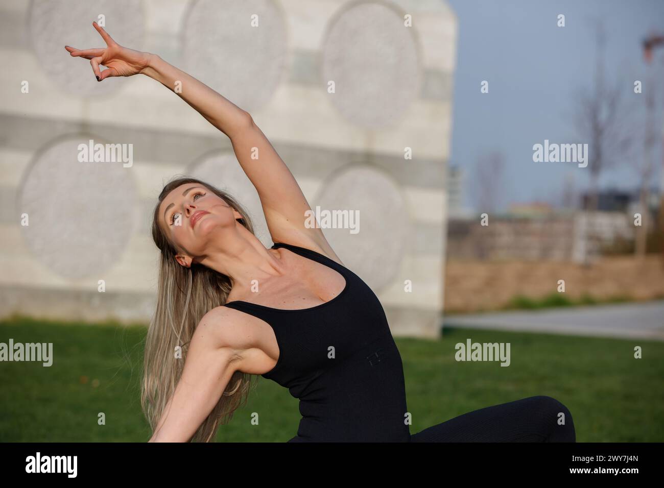 Ein wunderschönes blondes Model und Yogalehrerin, das Yoga im CityLife Park vor der Coloris Skulptur CityLife, Mailand, Italien macht Stockfoto