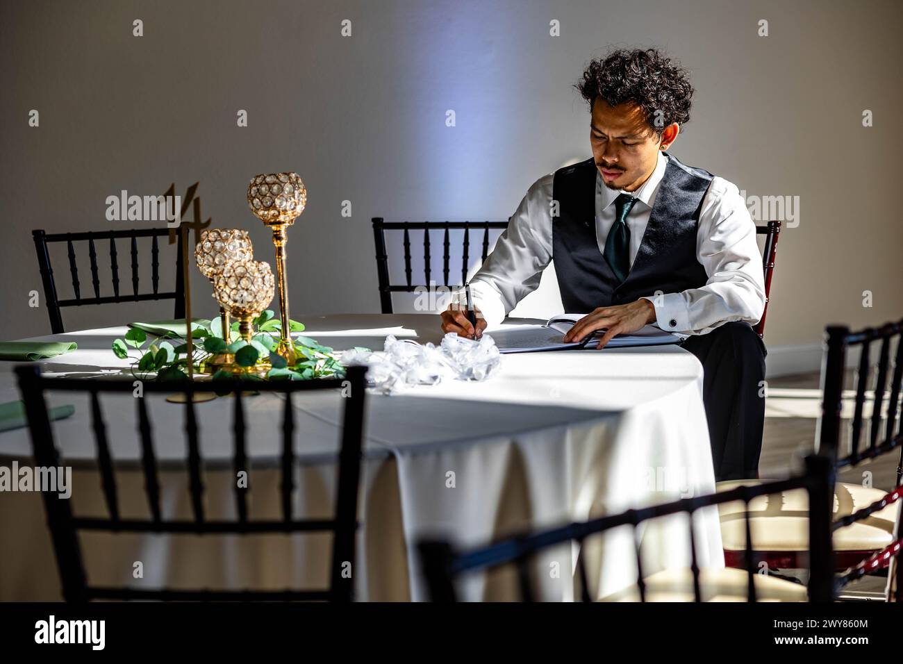 Bräutigam in schwarzer Weste unterschreibt Hochzeitsgelübde, mit Blumen auf dem Tisch im Hintergrund Stockfoto