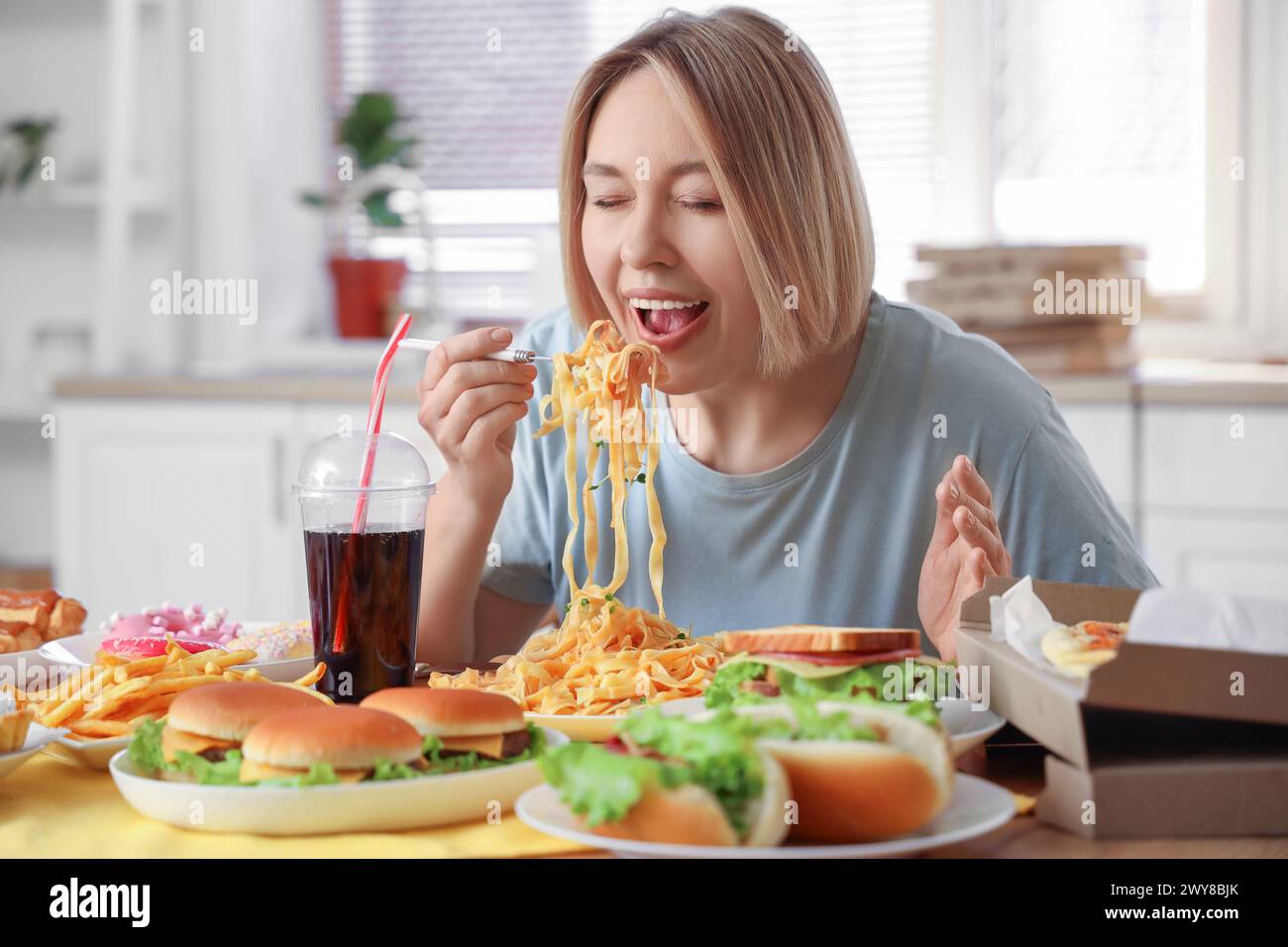 Schöne Frau mit leckeren Nudeln am Tisch in der Küche. Das Konzept des Überessens Stockfoto
