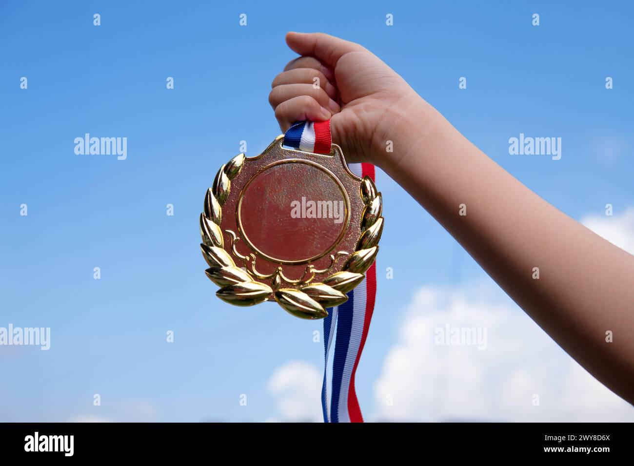 Eine Hand hält triumphierend eine Goldmedaille hoch oben vor dem Hintergrund des klaren blauen Himmels. Kopierbereich für Text. Gewinner, Erfolg und Erfolgskonzept. Stockfoto