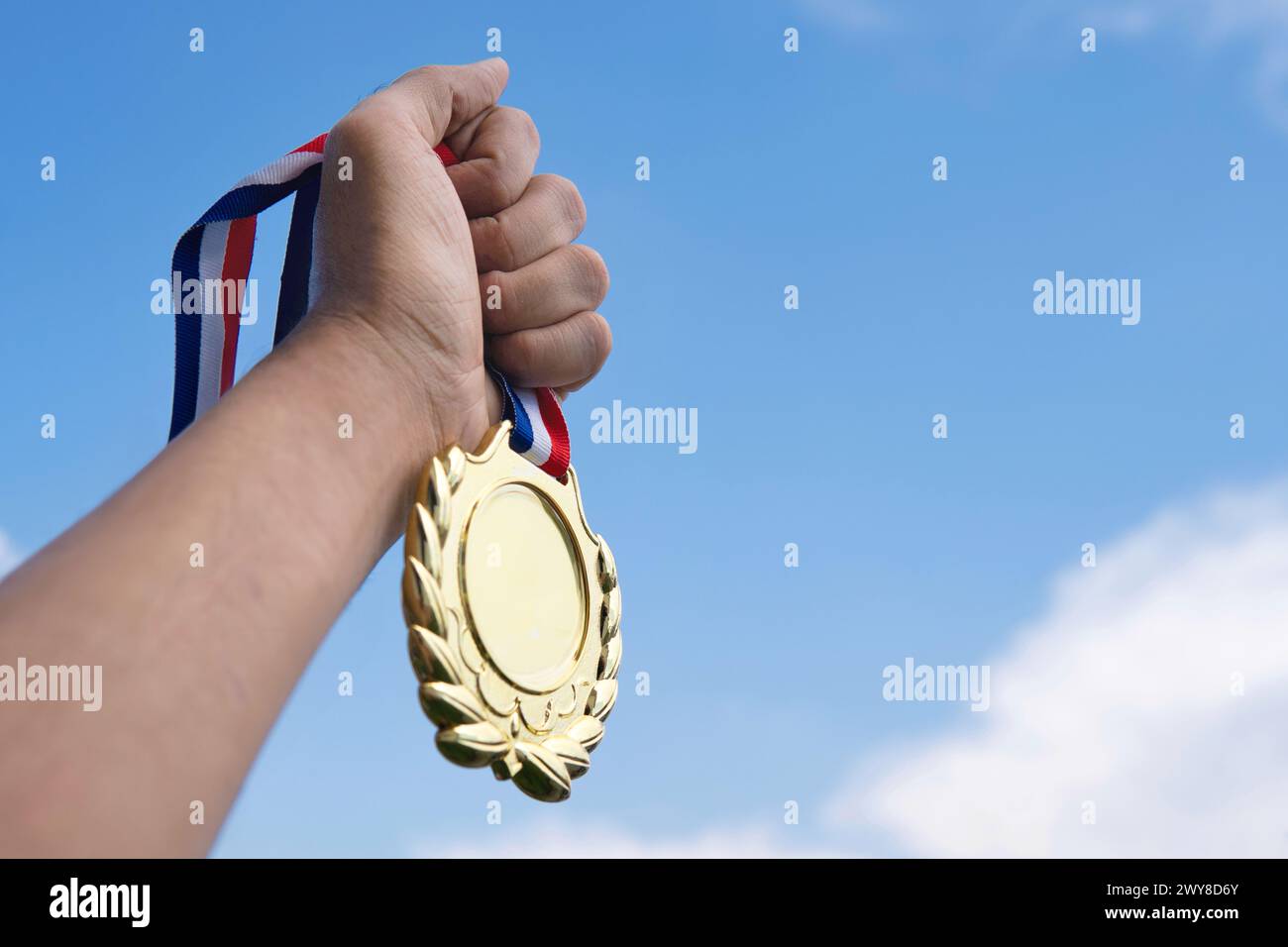 Eine Hand hält triumphierend eine Goldmedaille hoch oben vor dem Hintergrund des klaren blauen Himmels. Kopierbereich für Text. Gewinner, Erfolg und Erfolgskonzept. Stockfoto